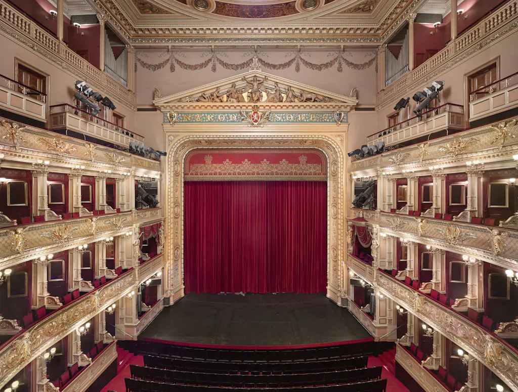 Ornate theater interior with red curtains, gold balconies, and multiple levels of seating