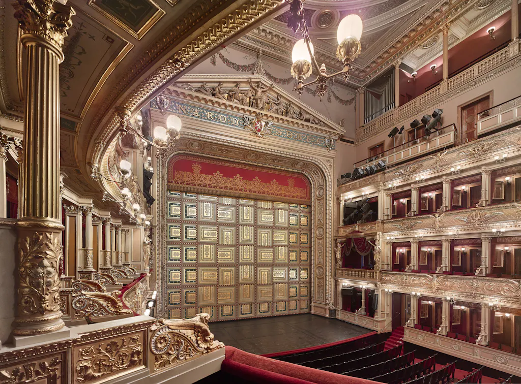 Ornate interior of the National Theatre with golden columns, red seats, and multiple balconies