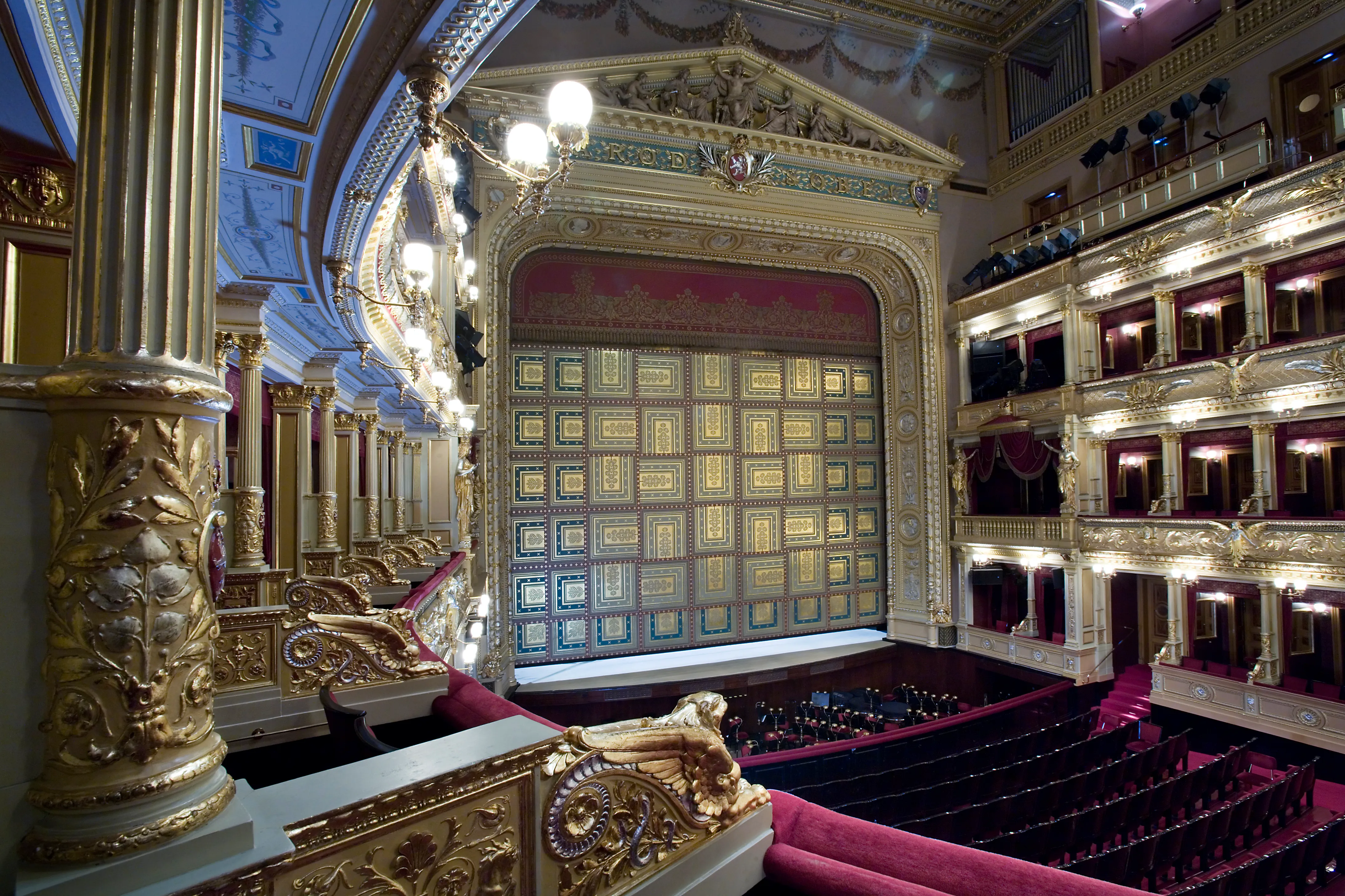 Ornate interior of the National Theatre with golden balconies, red seats, and a large stage curtain.