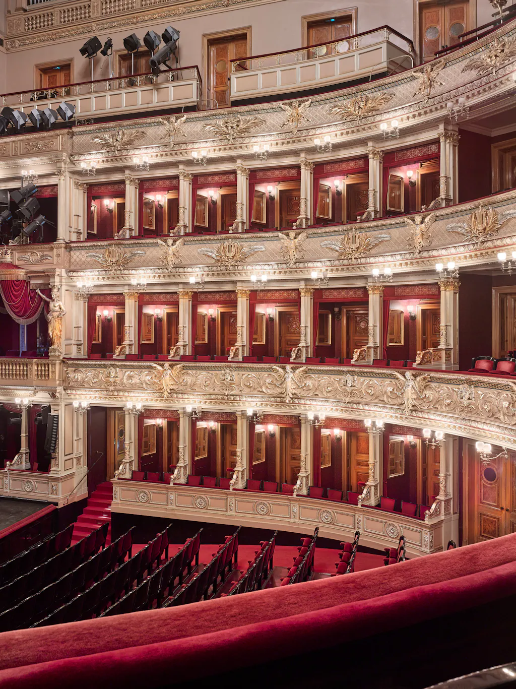 Ornate interior of the National Theatre with multiple levels of balconies, red seats, and gold decorative elements.