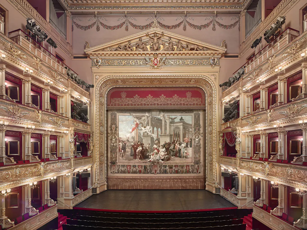 Ornate theater interior with gold detailing, red seats, and a large stage curtain