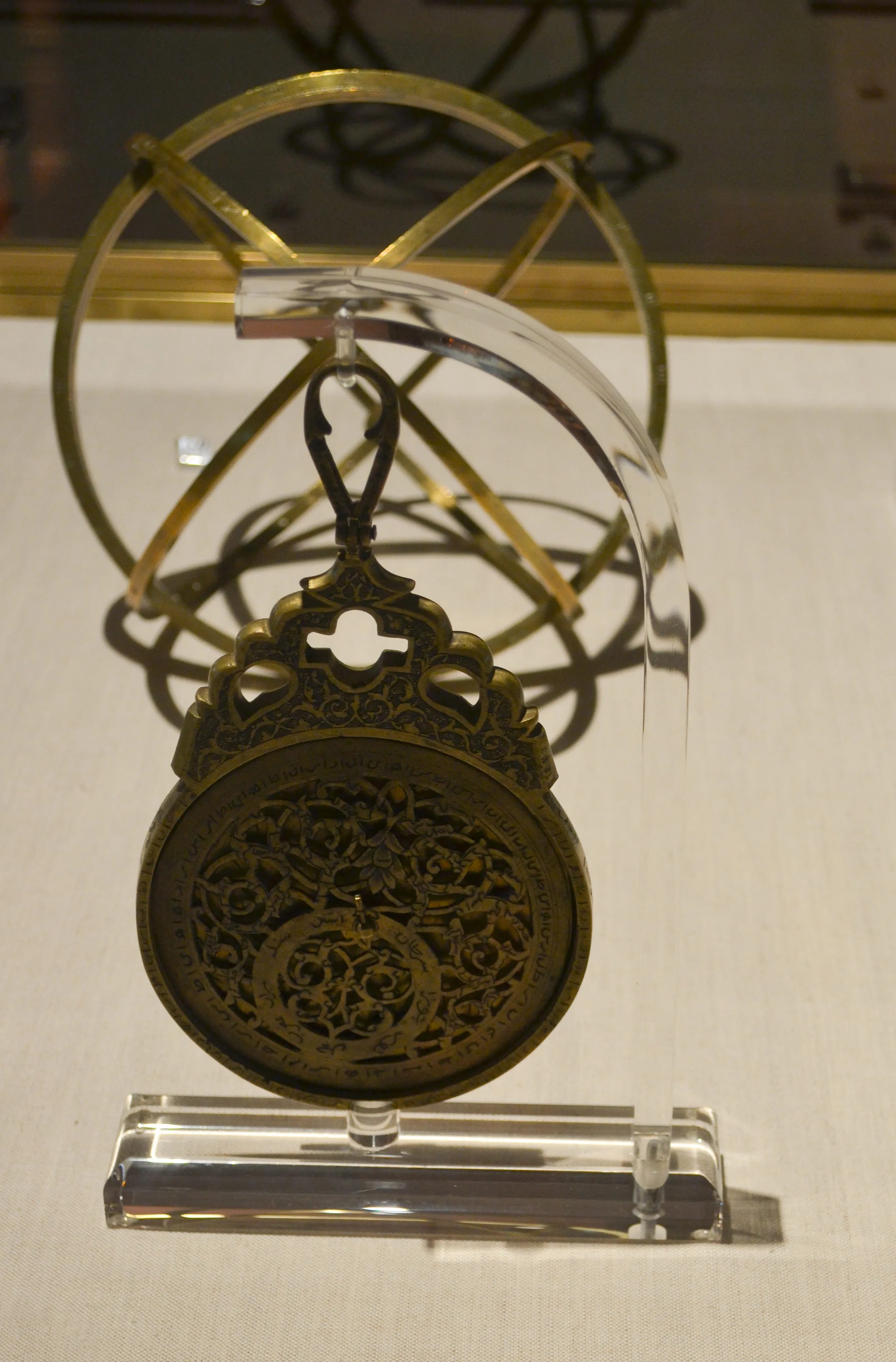 Bronze astrolabe with intricate engravings displayed on a clear stand