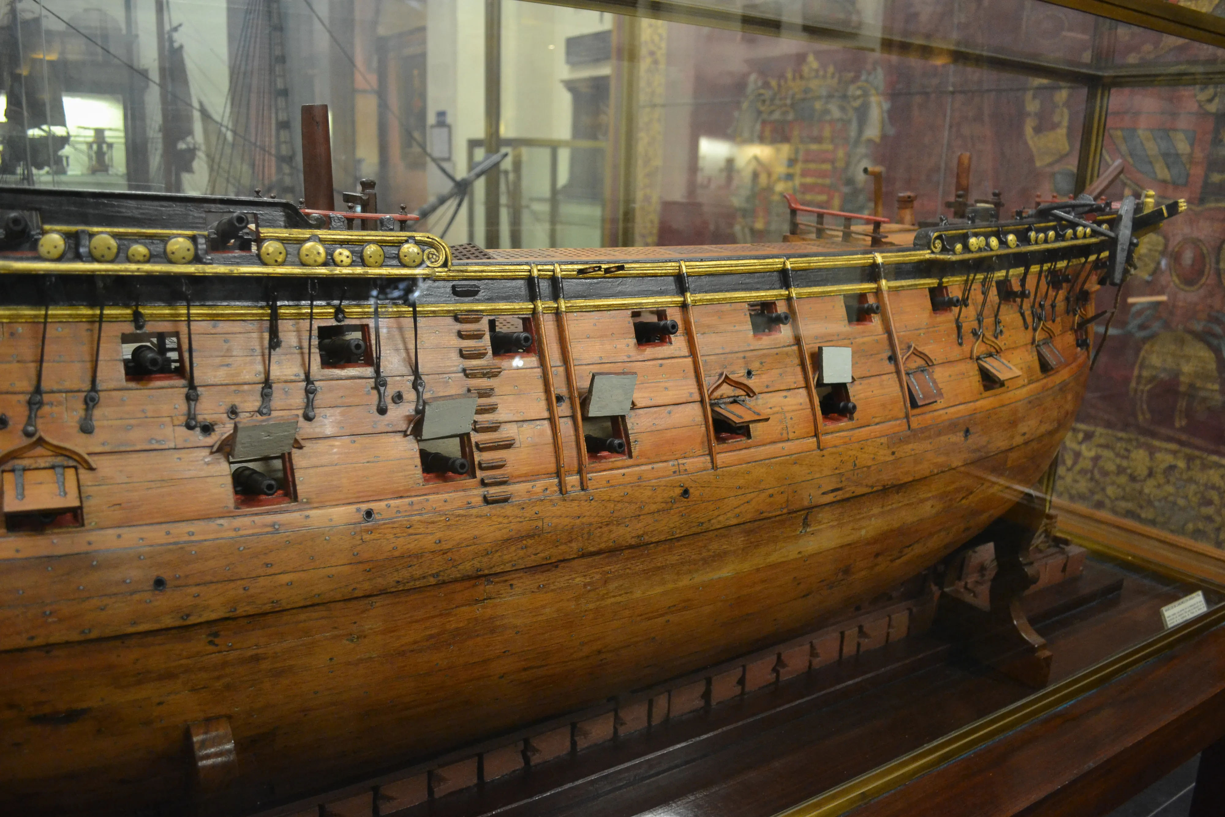 wooden model of a historical ship with cannons and rigging inside a glass case