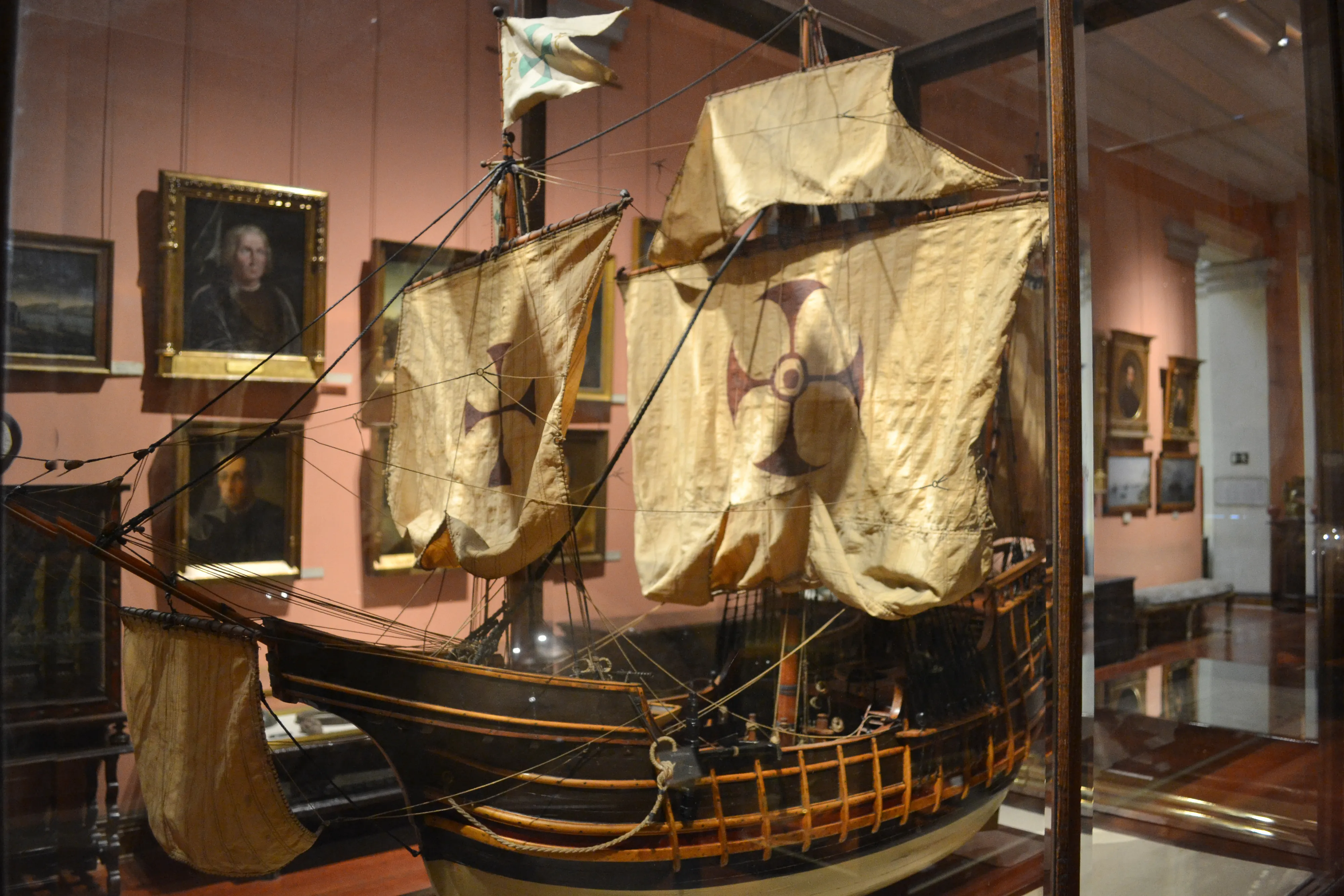 Model of a ship with tan sails and a cross emblem inside a glass case at the Naval Museum