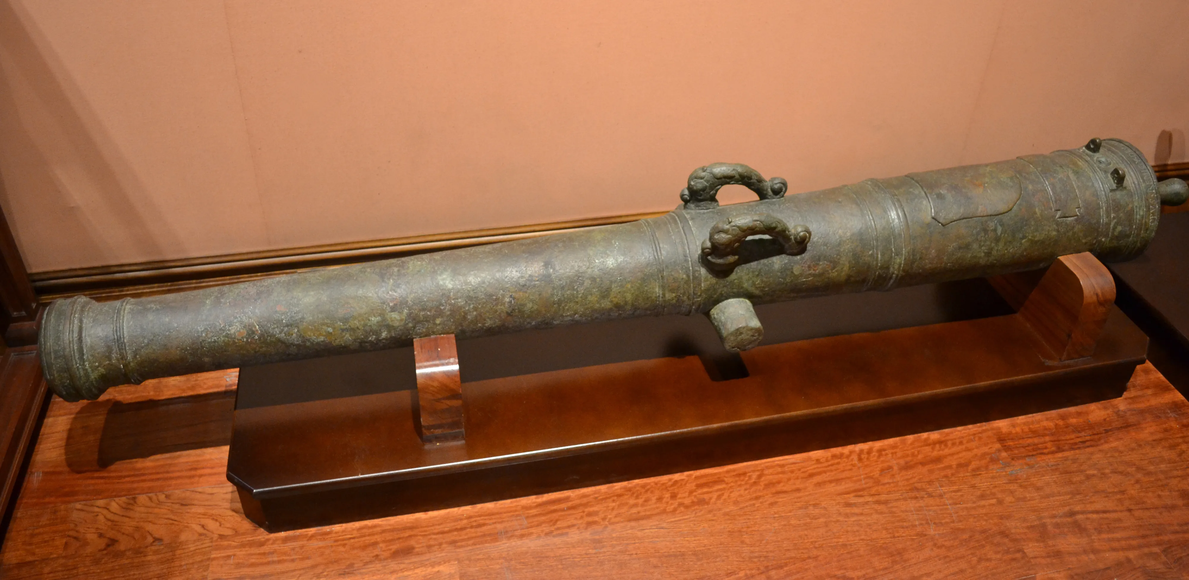 bronze cannon on wooden stand inside glass case
