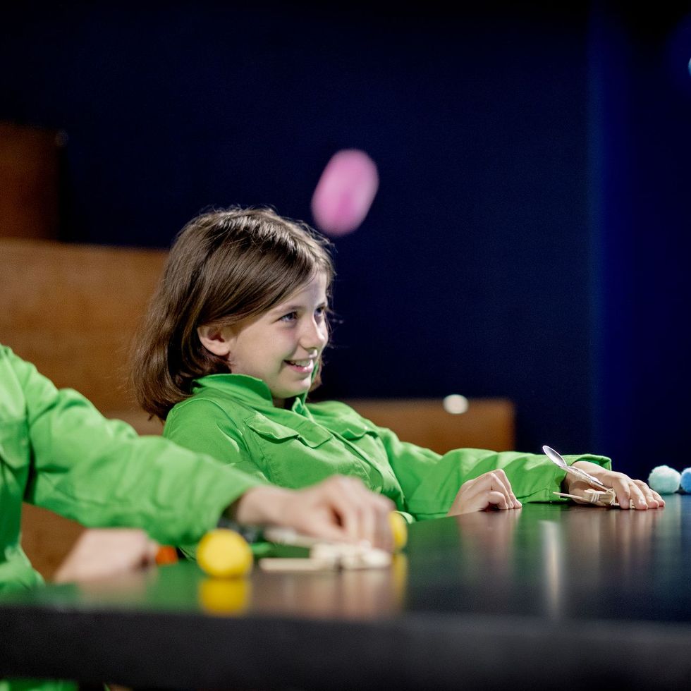 Kind in groen shirt dat interacteert met kleurrijke ballen aan een interactieve wetenschapstafel met donkere achtergrond