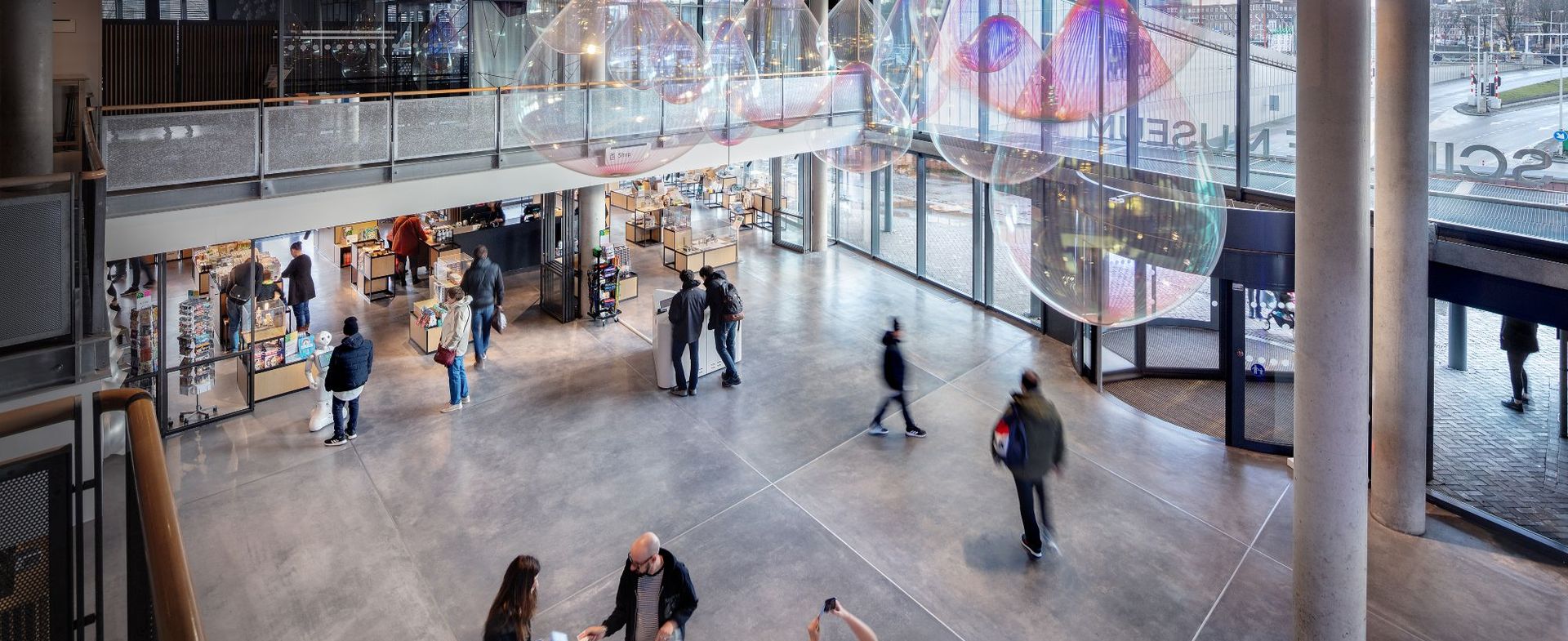 Spacious interior of NEMO Science Museum with visitors exploring exhibits, large windows, and modern architectural elements including a suspended installation