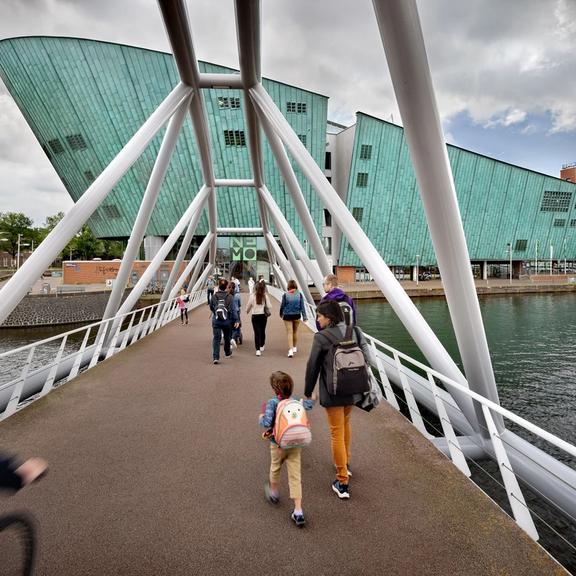 Bridge leading to NEMO Science Museum's modern green building with visitors walking toward the entrance over water