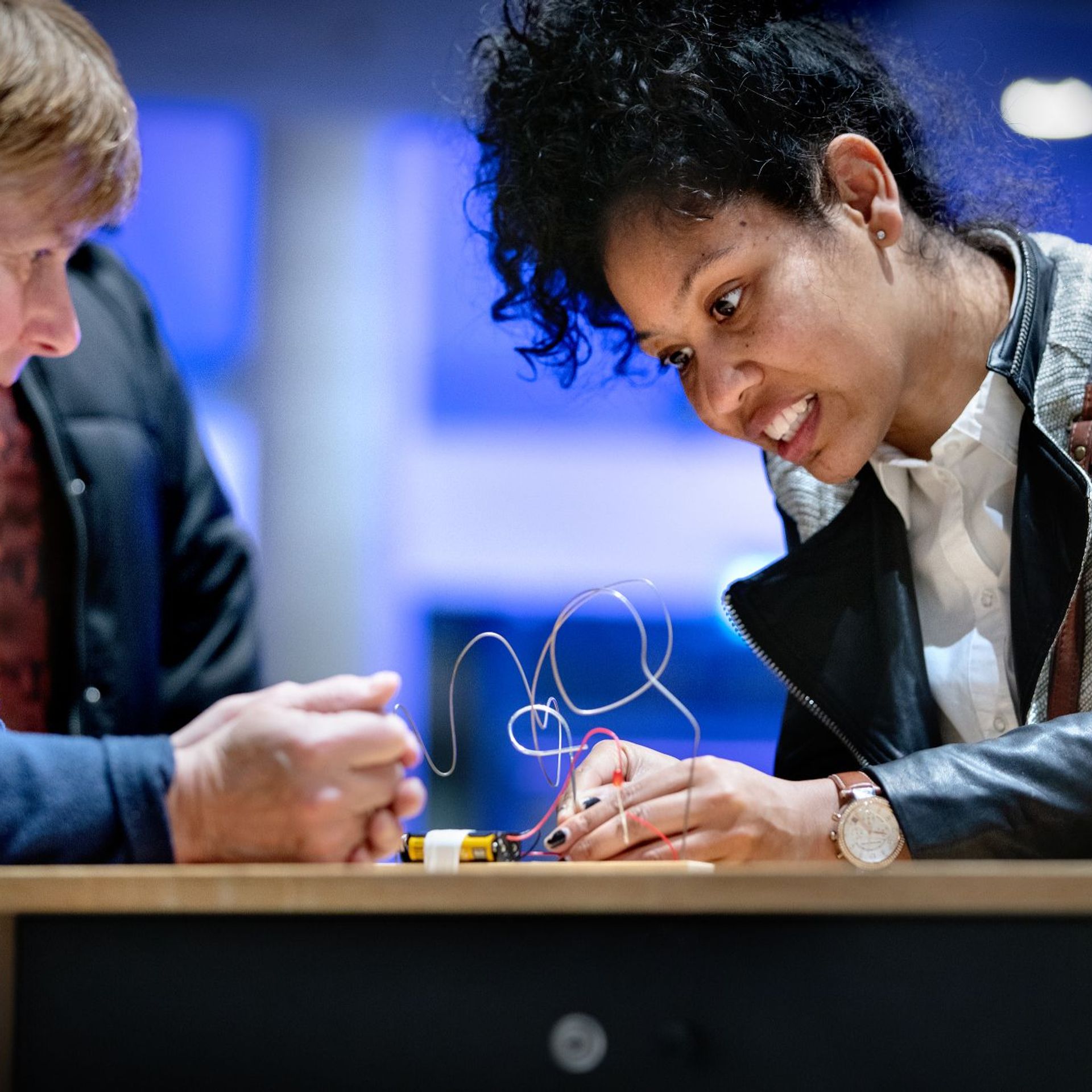 Twee bezoekers werken samen aan een interactieve draadpuzzeltentoonstelling met kleurrijke onderdelen en moderne verlichting.
