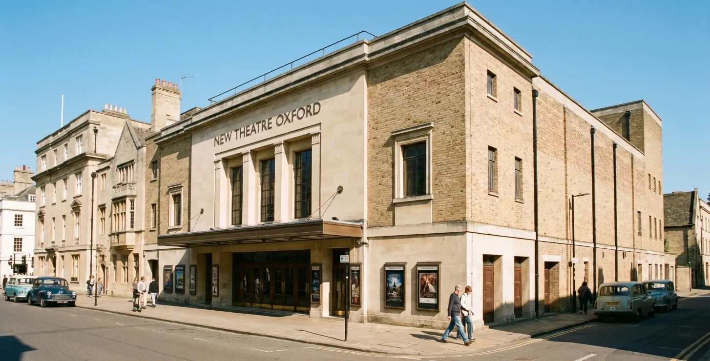 Widok z poziomu ulicy na fasadę budynku New Theatre Oxford z nazwą umieszczoną nad wejściem, w otoczeniu sąsiednich budynków i zaparkowanych samochodów.