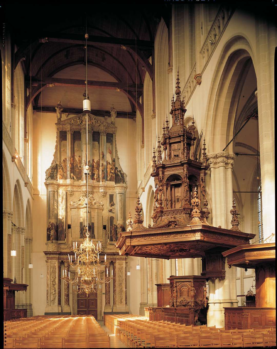 Interieur van de Nieuwe Kerk Amsterdam met een sierlijke houten preekstoel, pijporgel, rijen banken en hoge gewelfde plafonds met kroonluchters