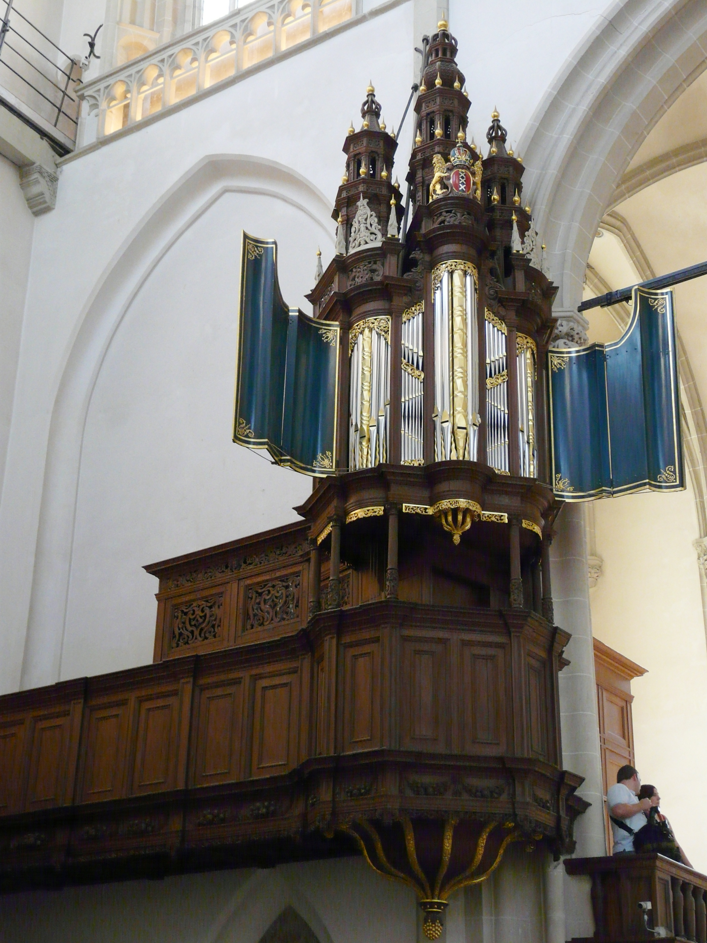 Ornate wooden pipe organ with gold accents and blue curtains inside a church