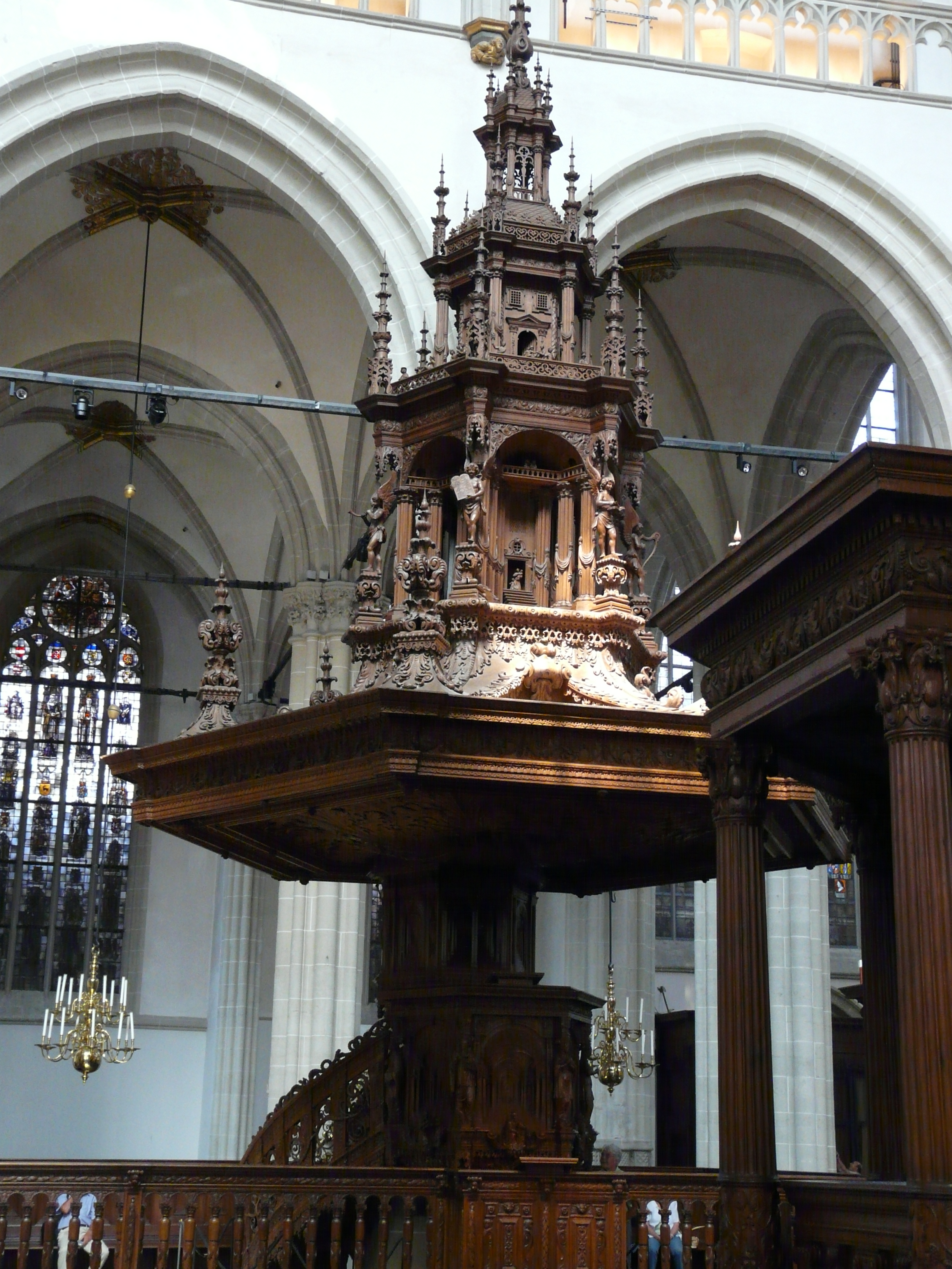 Ornates houten preekstoel met ingewikkelde houtsnijwerken binnen een kerk met gewelfde plafonds en glas-in-loodramen