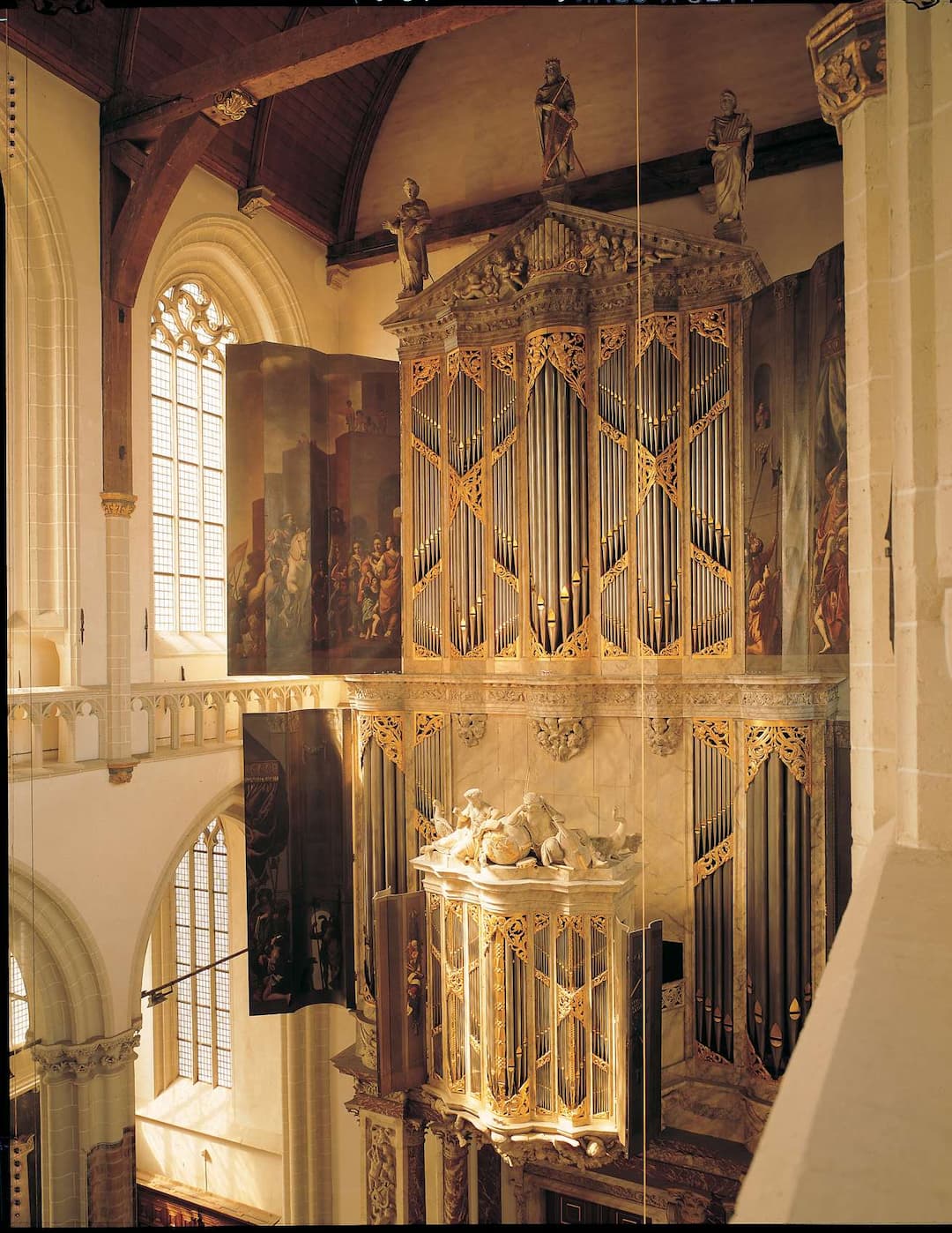 Interieur van de Nieuwe Kerk Amsterdam met een sierlijk gouden orgel, boogvensters met glas-in-lood en historische schilderijen aan de muren