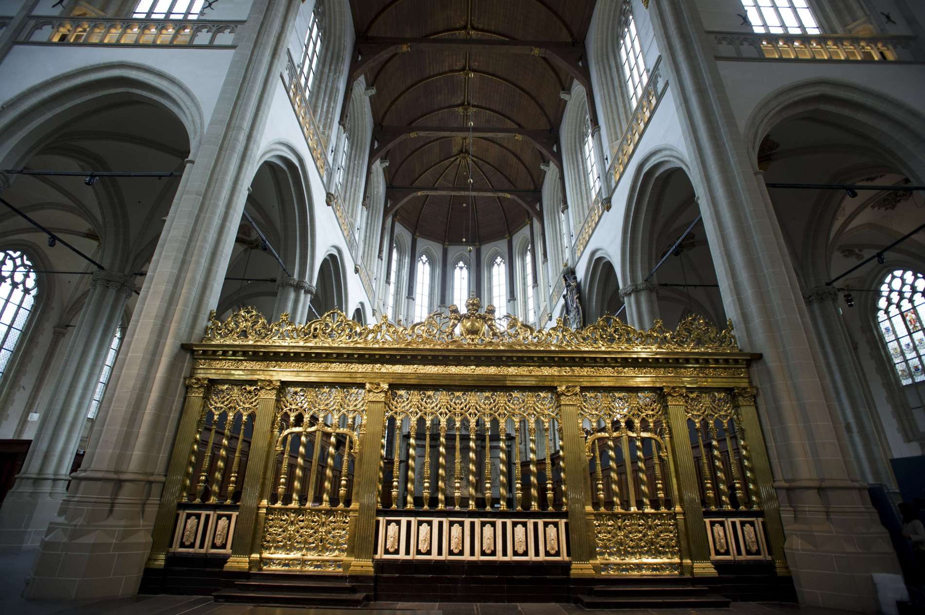 Grandioos interieur van een historische kerk met een groot, sierlijk, gouden orgel, boogramen, stenen zuilen en een gewelfd plafond met houten balken.