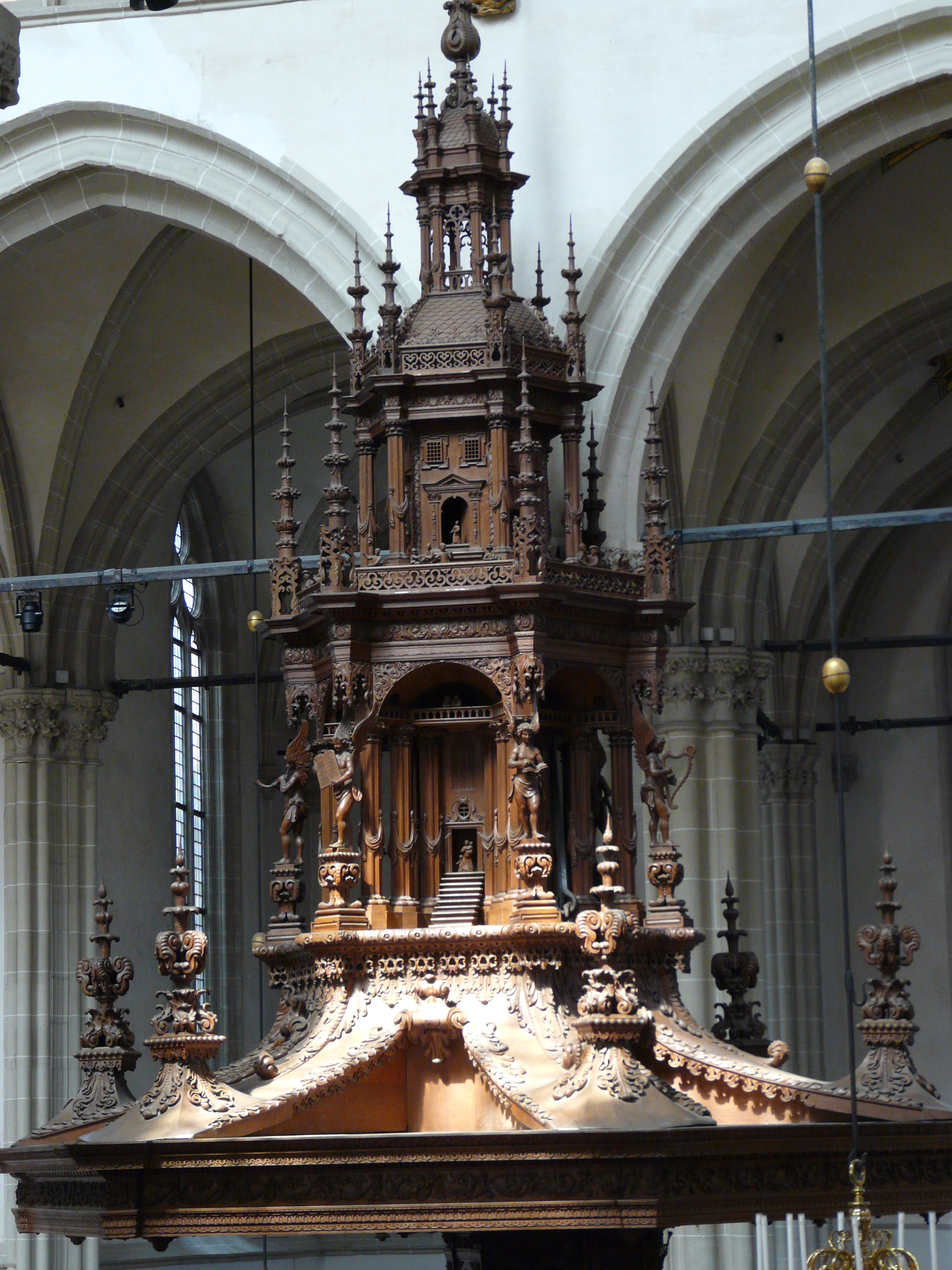 Gedetailleerd gesneden houten preekstoel met spitsen en beelden in de Nieuwe Kerk Amsterdam, met gewelfde stenen muren en sierlijke details