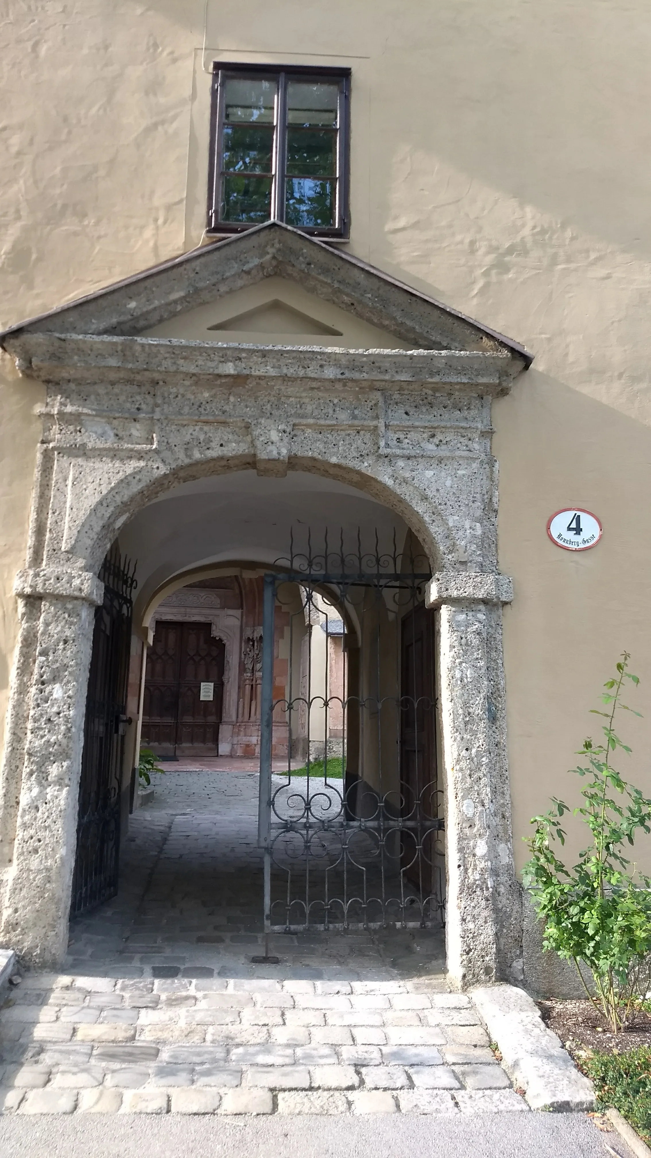 Stone arched entrance gate of Nonnberg Abbey with triangular pediment, wrought-iron gates, and cobblestone path leading through to a courtyard.