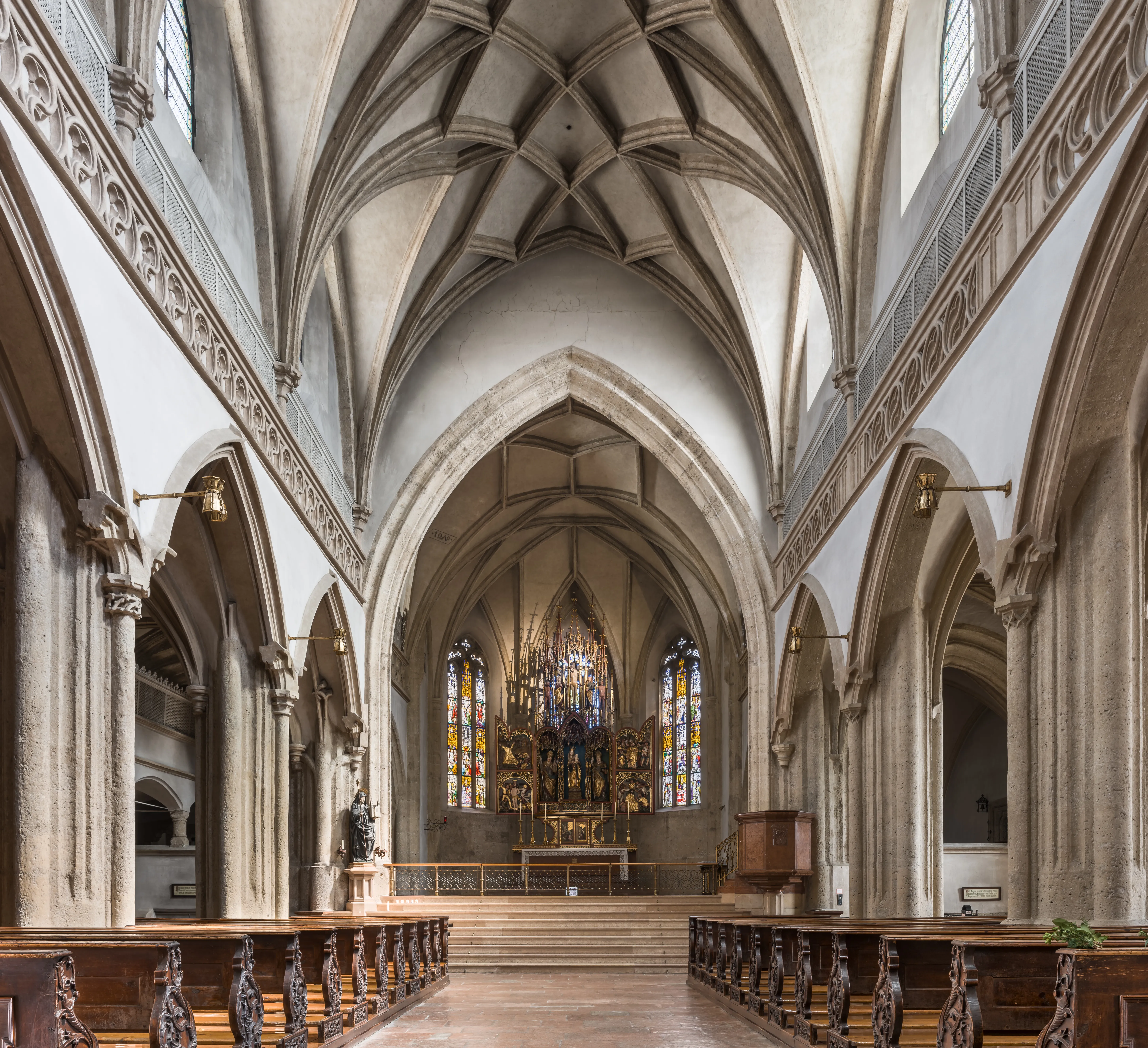 Interior view of Nonnberg Abbey church showing Gothic ribbed vaulted ceiling, arched stone nave columns, wooden pews, and stained glass altar at the far end.