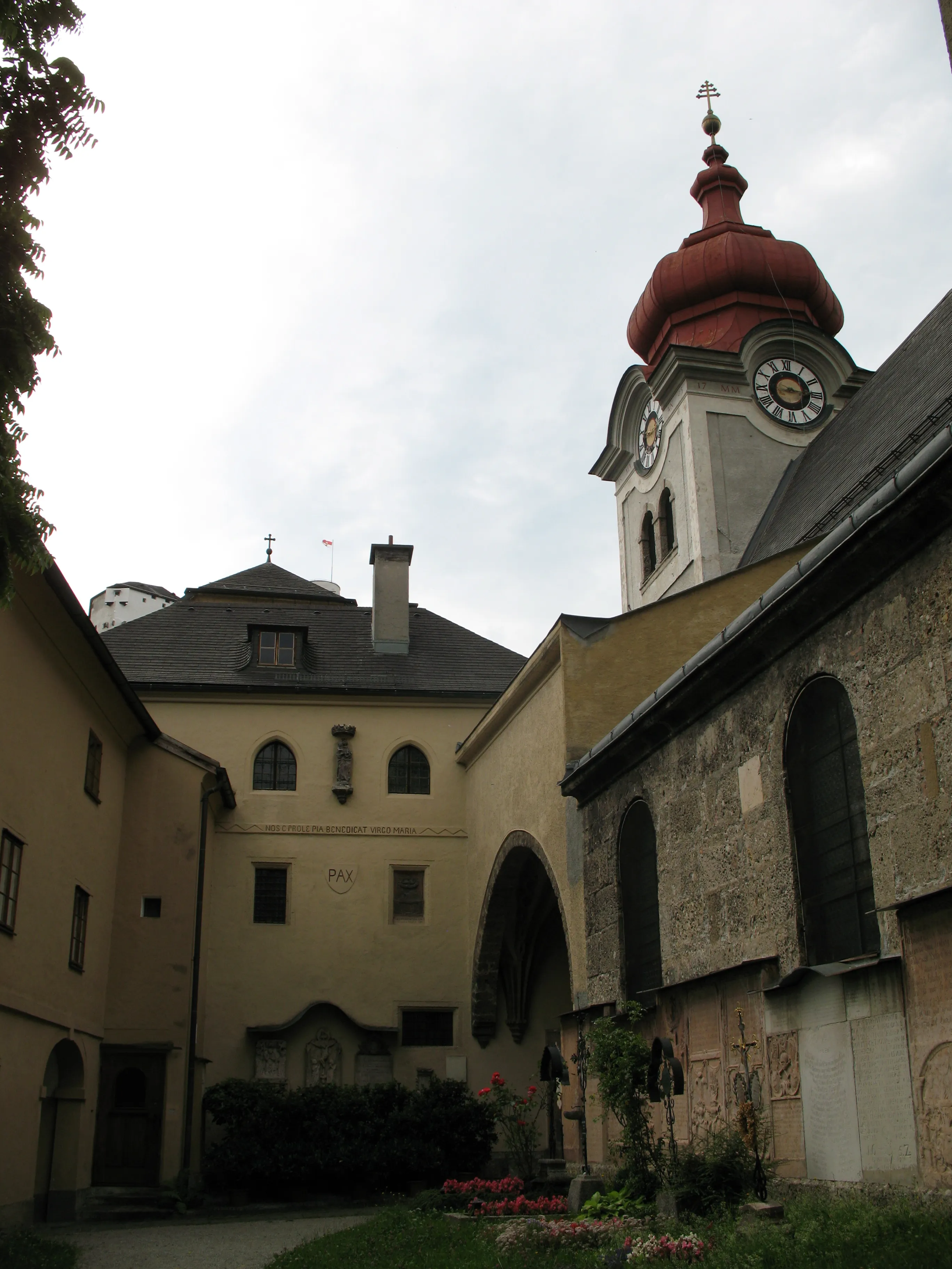 Courtyard of Nonnberg Abbey showing historic stone buildings and a church tower with a red onion dome and clock face