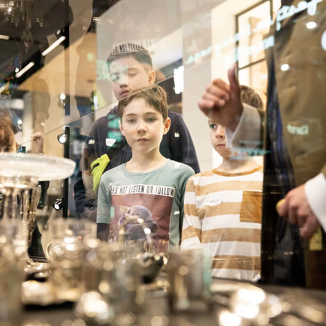 niños mirando una vitrina de cristal con cubertería y objetos de metal