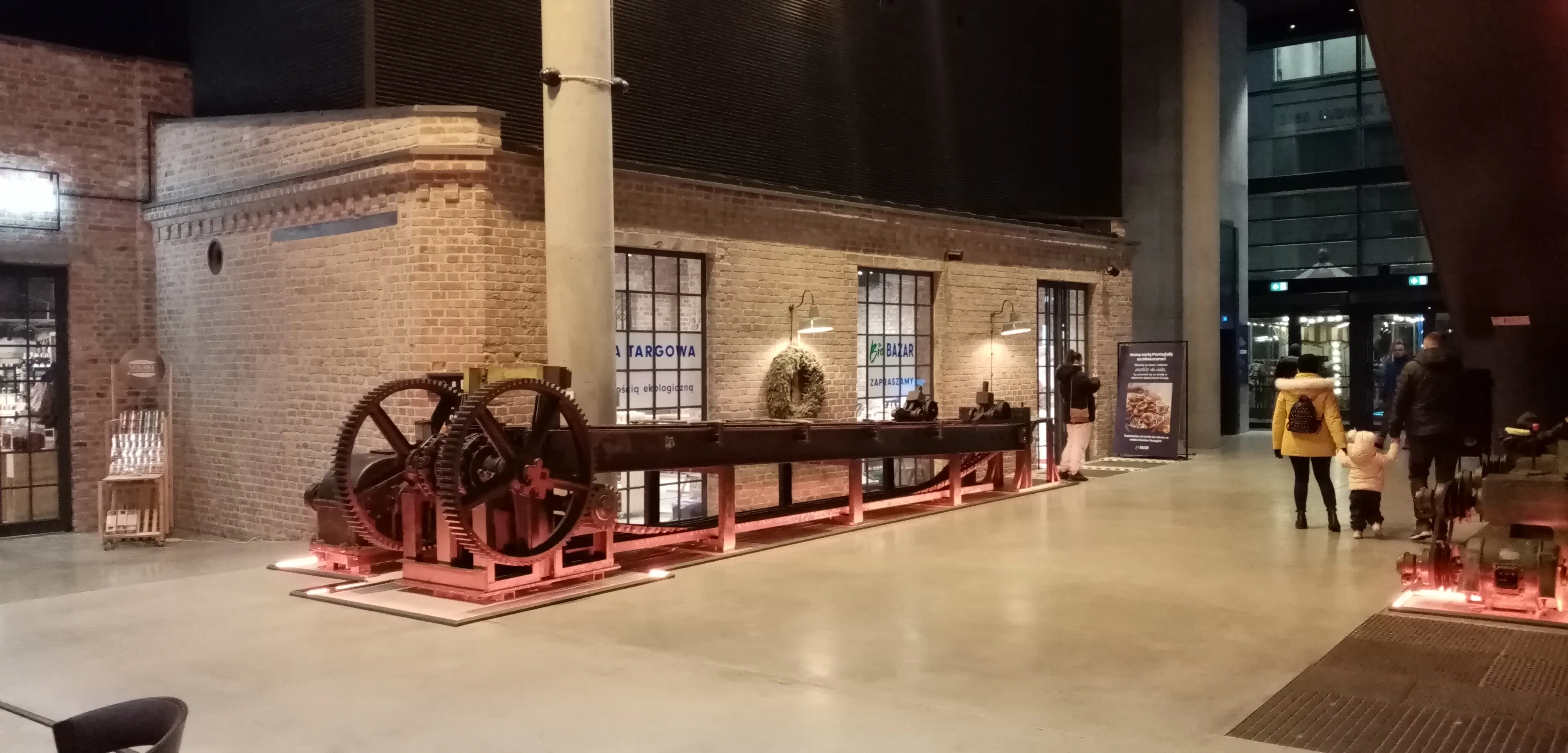 Máquina industrial en exhibición en un museo con paredes de ladrillo y visitantes