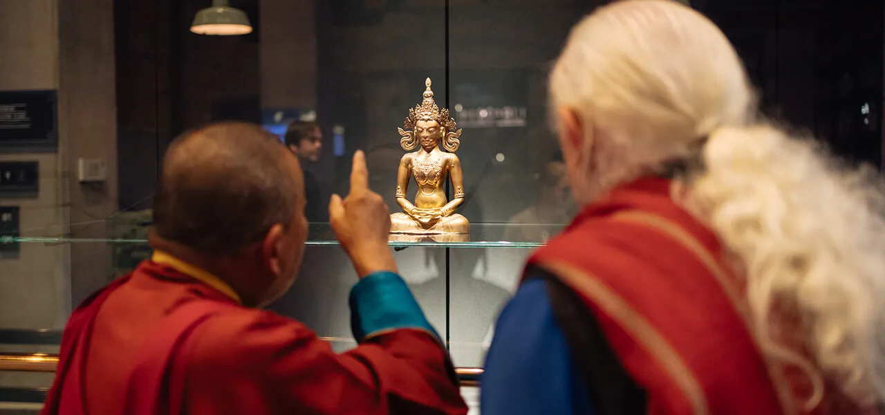 Dos personas viendo una estatua dorada de Buda en una vitrina de cristal