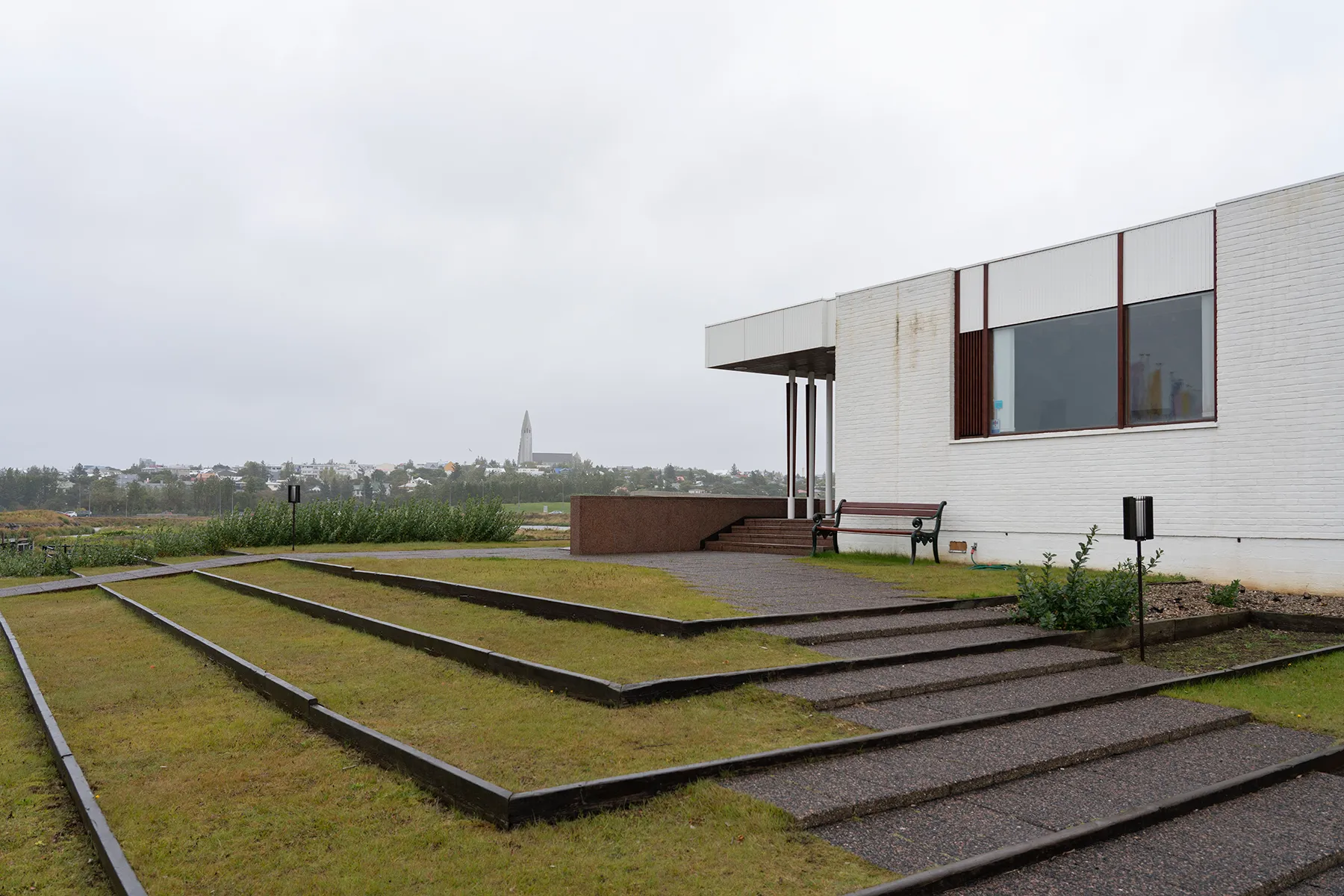 Exterior view of the Nordic House in Reykjavík showing white building with large windows, terraced grass steps, and city skyline with church spire in the background