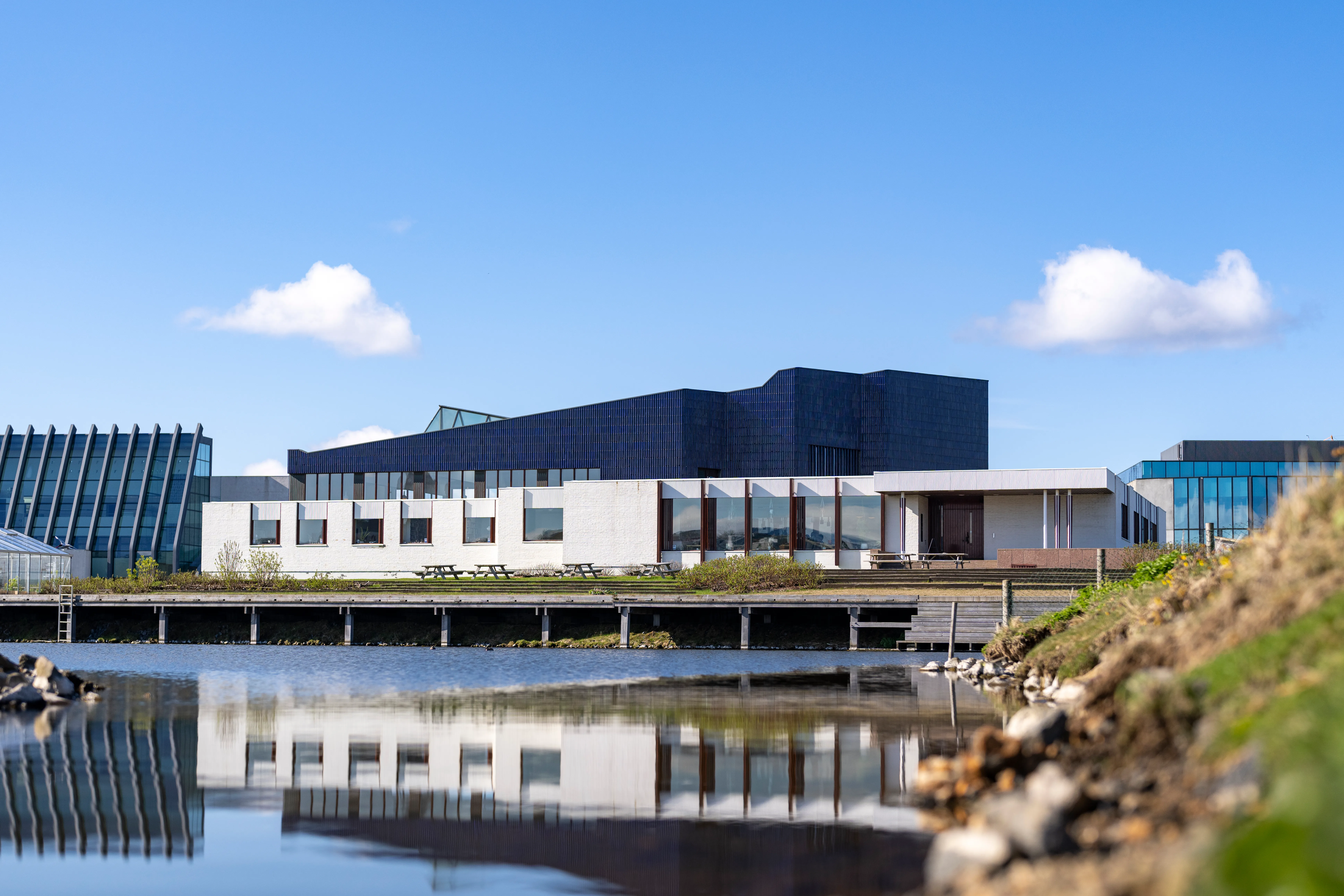 The Nordic House in Reykjavik with its distinctive dark angular roof and white facade reflected in a pond on a sunny day