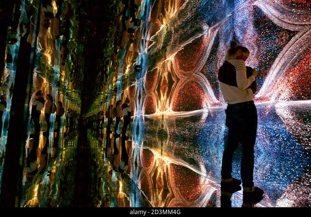 Vibrant digital art installation with swirling colorful patterns and light trails reflected on a glossy floor, people observing