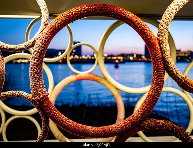Close-up of interlocking circular textured installations with a blurred cityscape and water at dusk in the background