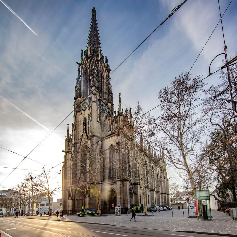 Neogotische kerk met een hoge, rijkelijk versierde toren, een stenen gevel en tramleidingen boven een stadsstraat