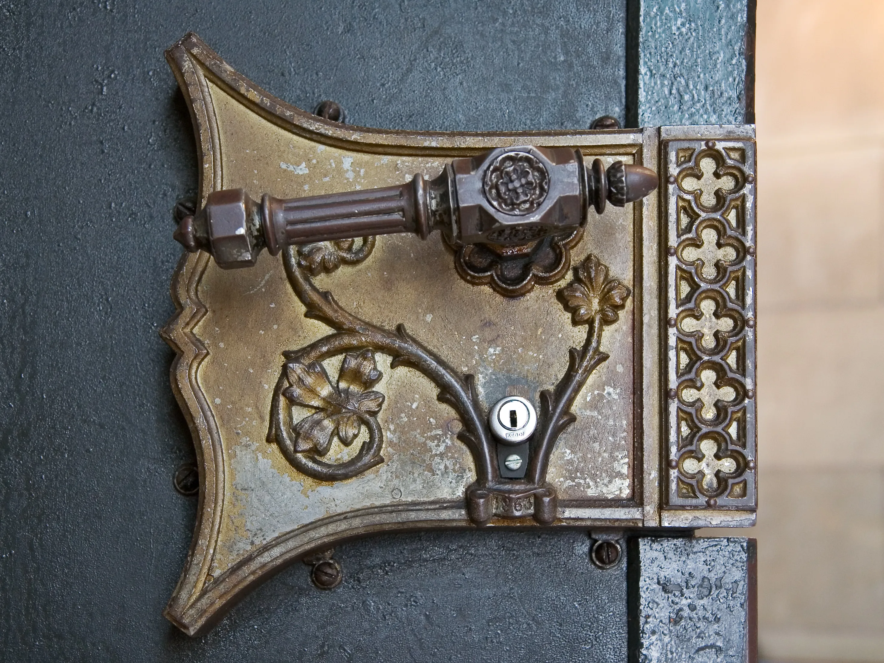 Rijkversierde bronzen deurklink en slotmechanisme met gotische bloemmotieven op een donkere kerkdeur