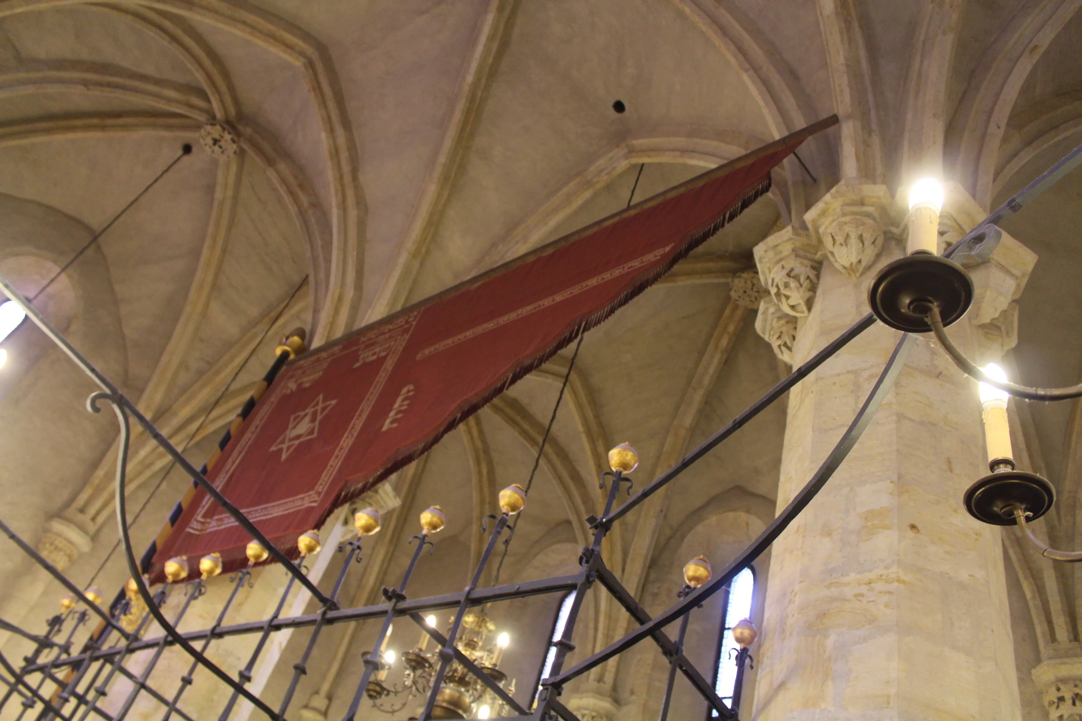 Interior de la Sinagoga Vieja-Nueva con techos abovedados, columnas de piedra y una pancarta roja colgada del techo