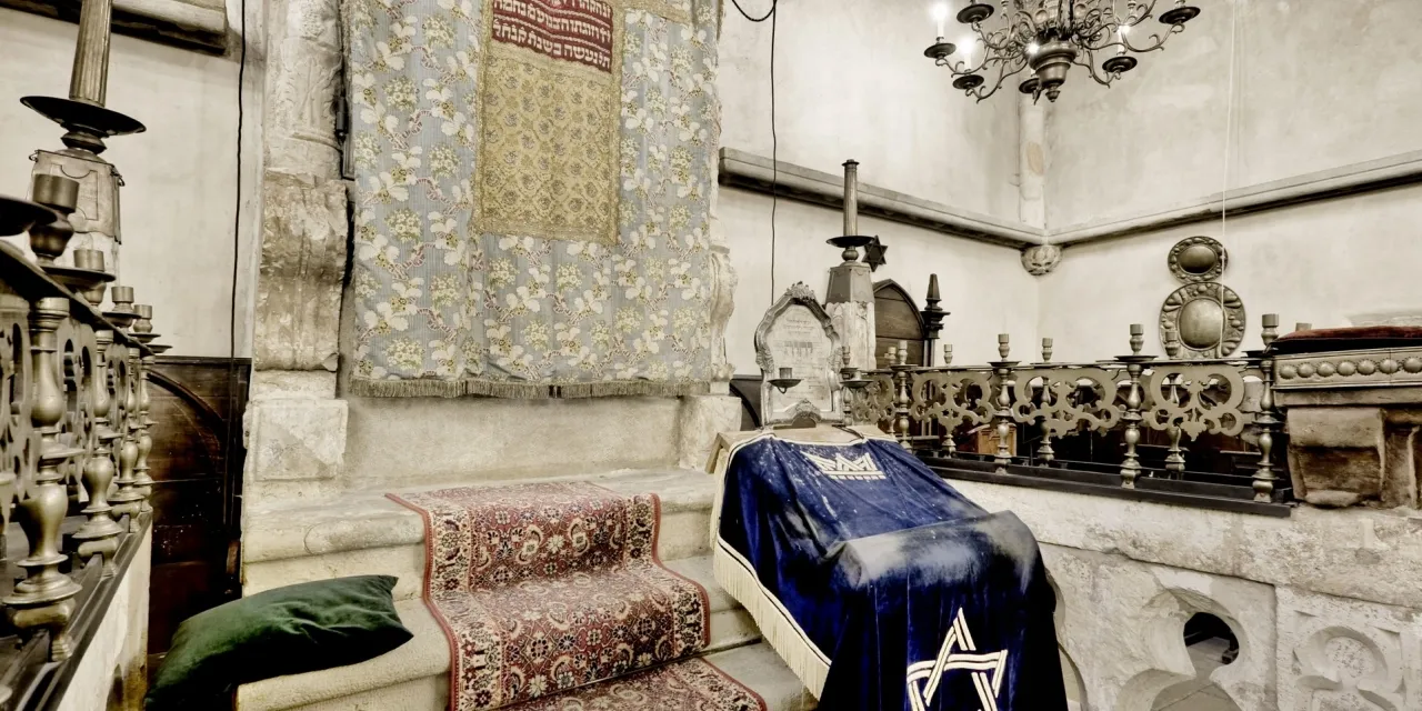 Interior de la Sinagoga Vieja-Nueva con un arca de Torá cubierta de terciopelo azul y una Estrella de David, candelabros y muros de piedra