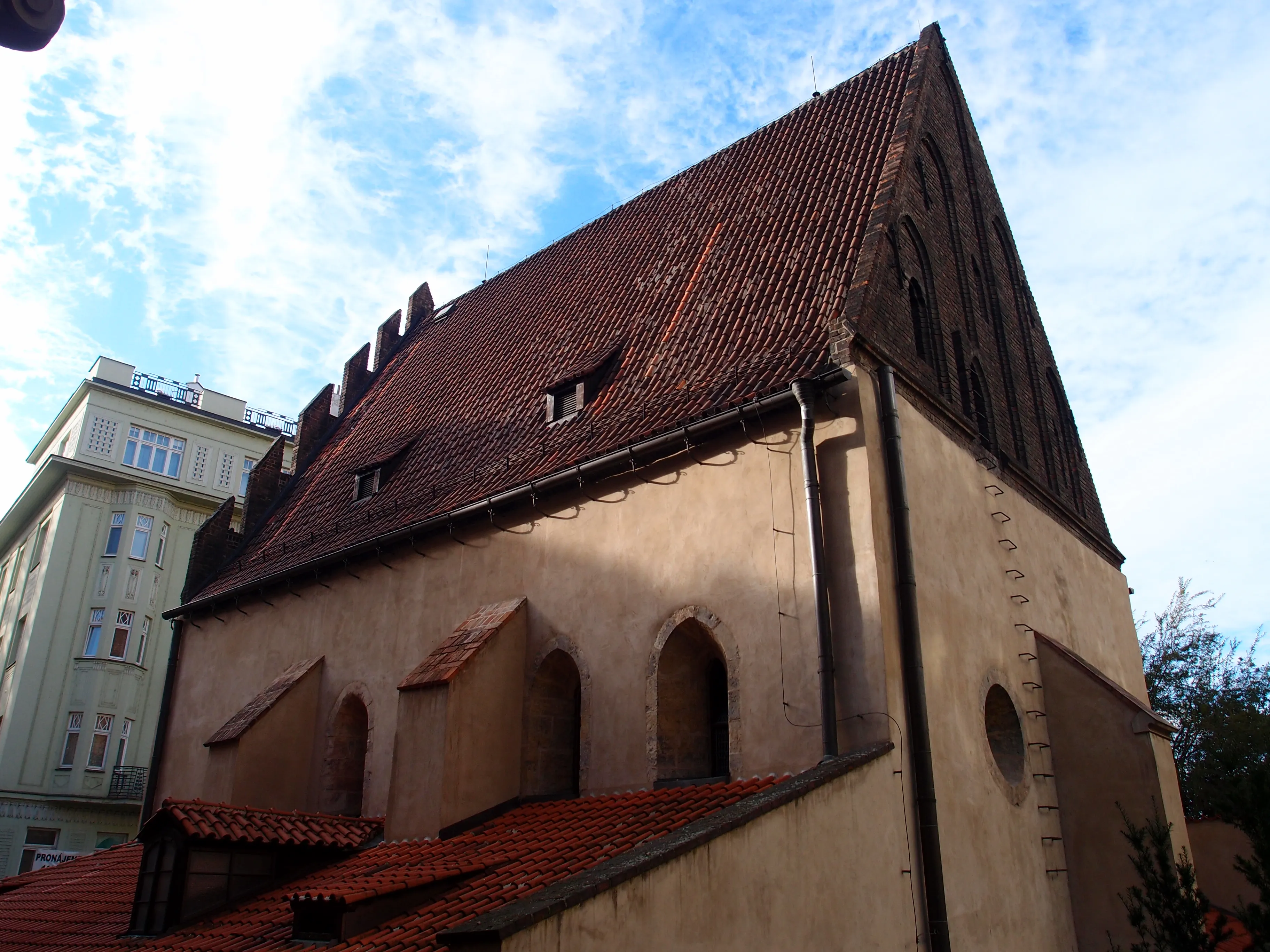 La Sinagoga Vieja-Nueva con un tejado de tejas rojas inclinado y ventanas arqueadas bajo un cielo azul