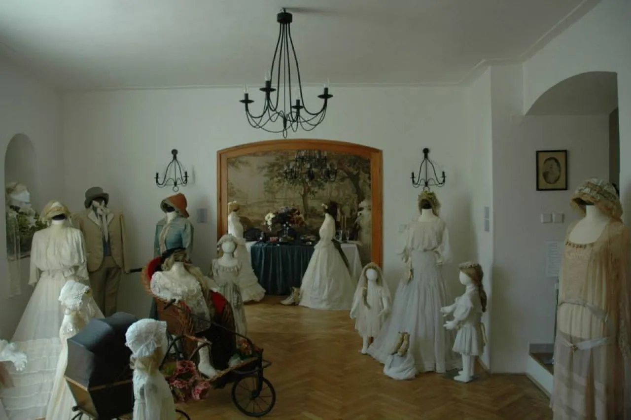 Maniquíes con ropa de época expuestos en una sala de museo con candelabro y suelos de madera