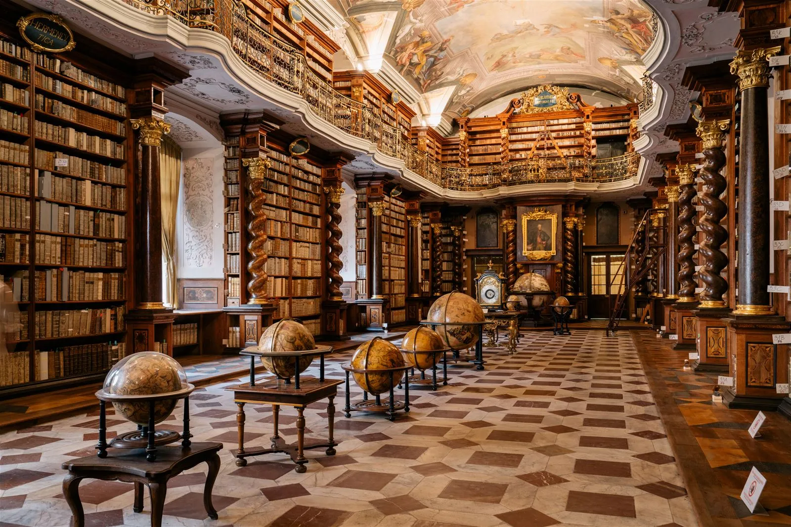 Ornate library interior with high wooden bookshelves, a decorated ceiling, and globes on tables