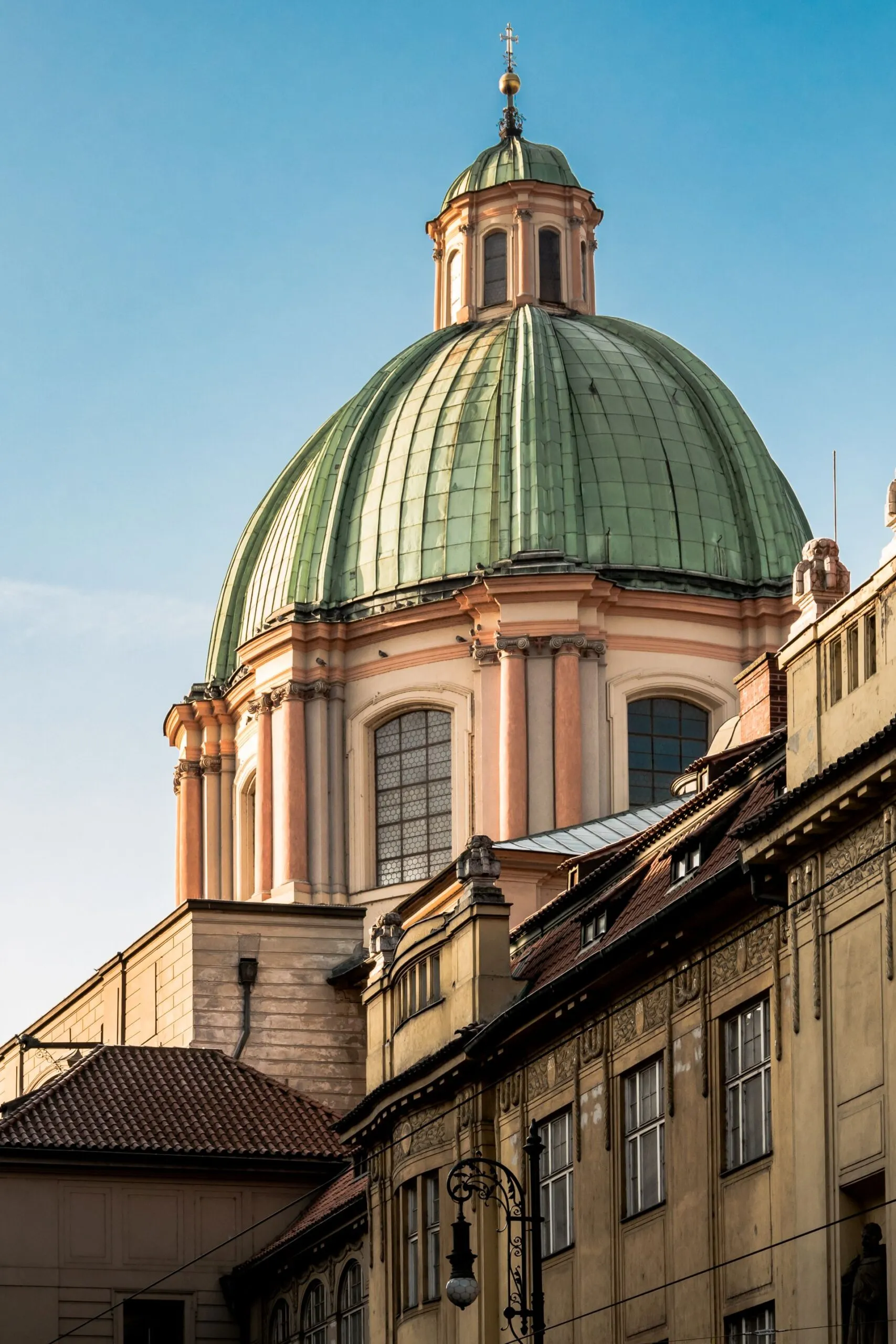 A green copper dome of the Old Town Bridge Tower with surrounding historic buildings under a clear blue sky
