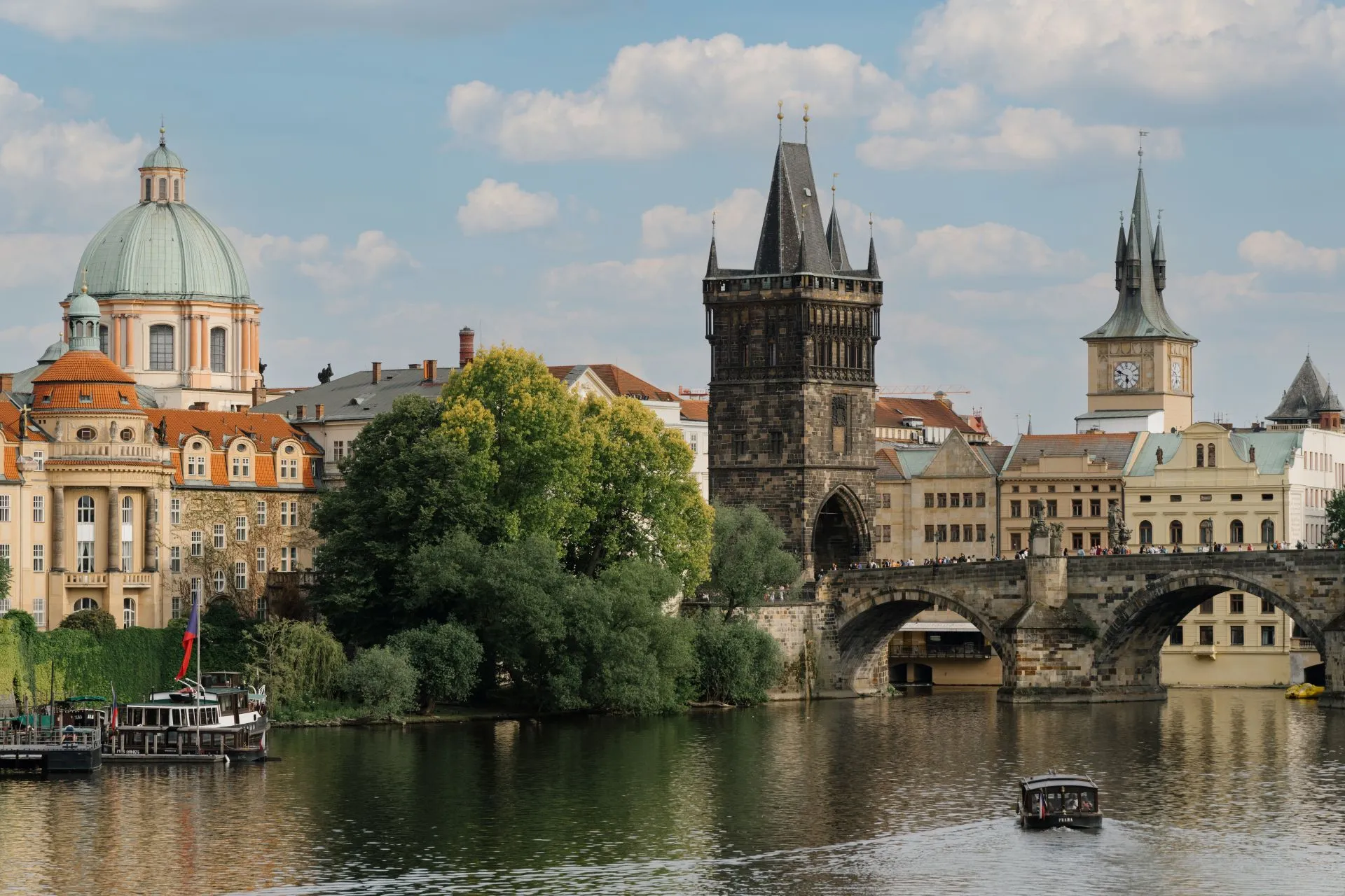 Gothic tower at the end of Charles Bridge with historic buildings and a river in the foreground