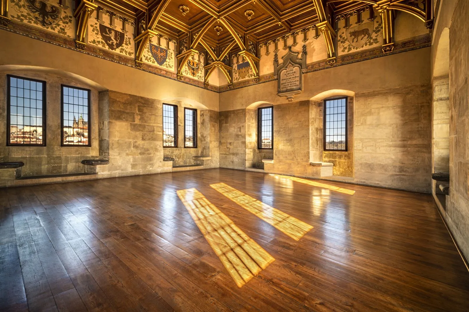 Interior of the Old Town Bridge Tower with stone walls, large windows, and sunlight casting geometric patterns on the wooden floor