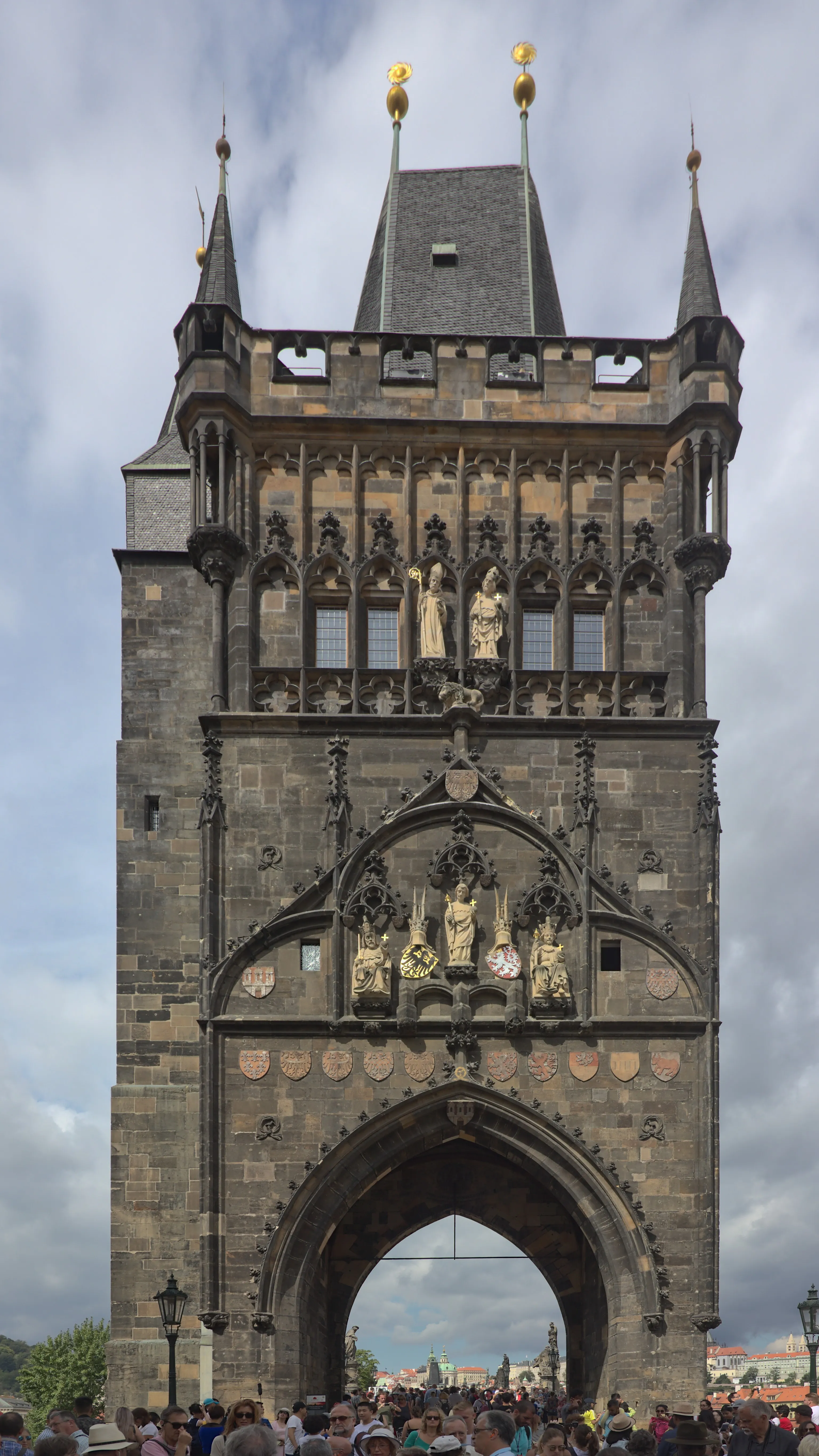 Gothic stone tower with spires and statues, featuring an arched gateway with people below