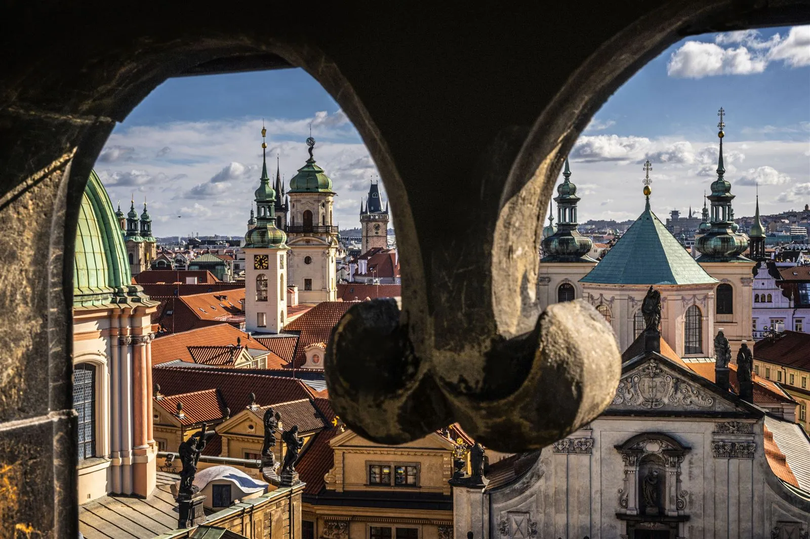Stone archway framing a panoramic view of Prague's historic rooftops and spires under a partly cloudy sky