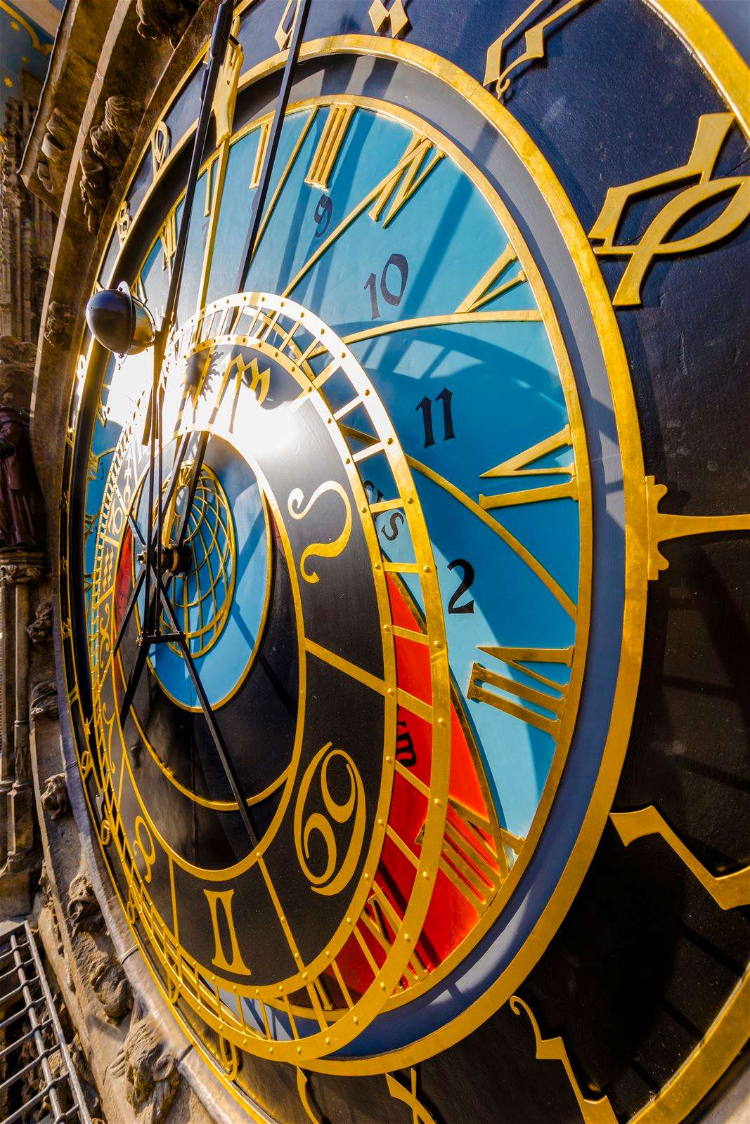 Zbliżenie na zegar astronomiczny z niebieskimi i czarnymi tarczami, złotymi wskazówkami i symbolami zodiaku