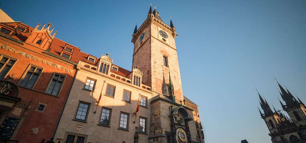 Zabytkowy budynek z wysoką wieżą zegarową i dachem z czerwonej dachówki pod czystym błękitnym niebem
