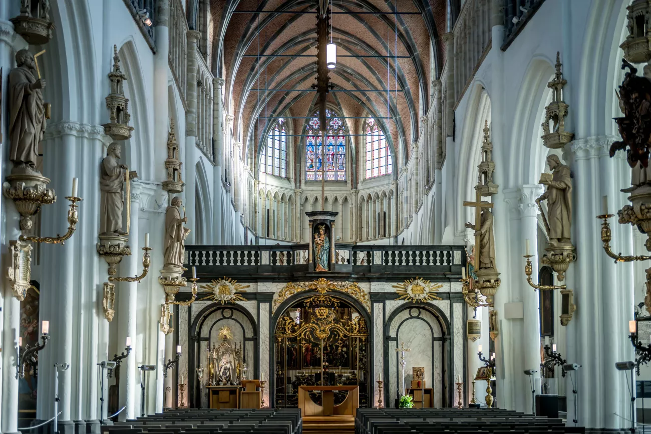 Vista interior de la nave de la Iglesia de Nuestra Señora con columnas blancas, estatuas, techo de ladrillo abovedado y un altar ornamentado y dorado