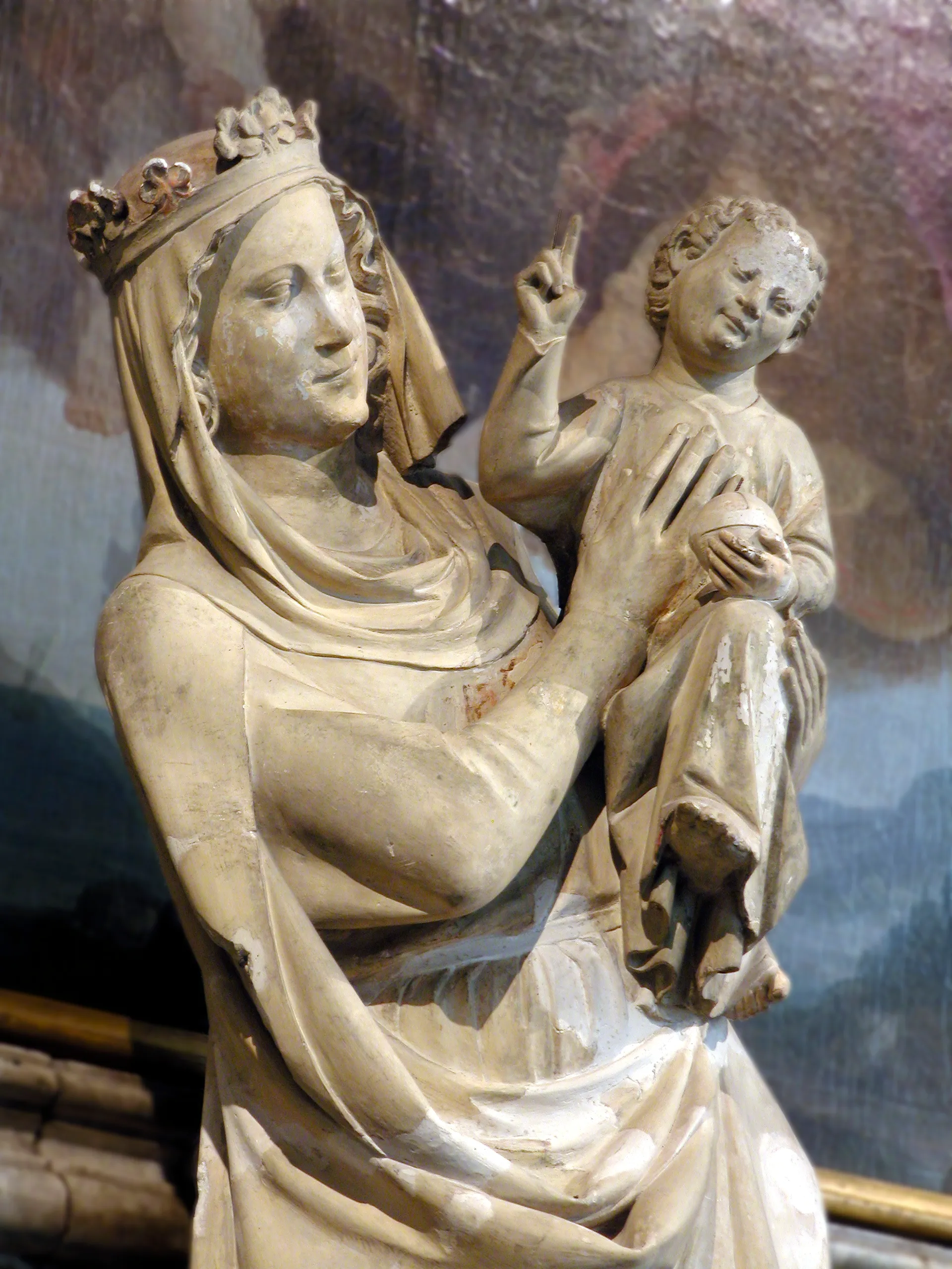 Escultura de piedra de la Virgen María con corona y velo, sosteniendo al Niño Jesús, quien levanta un dedo en señal de bendición.