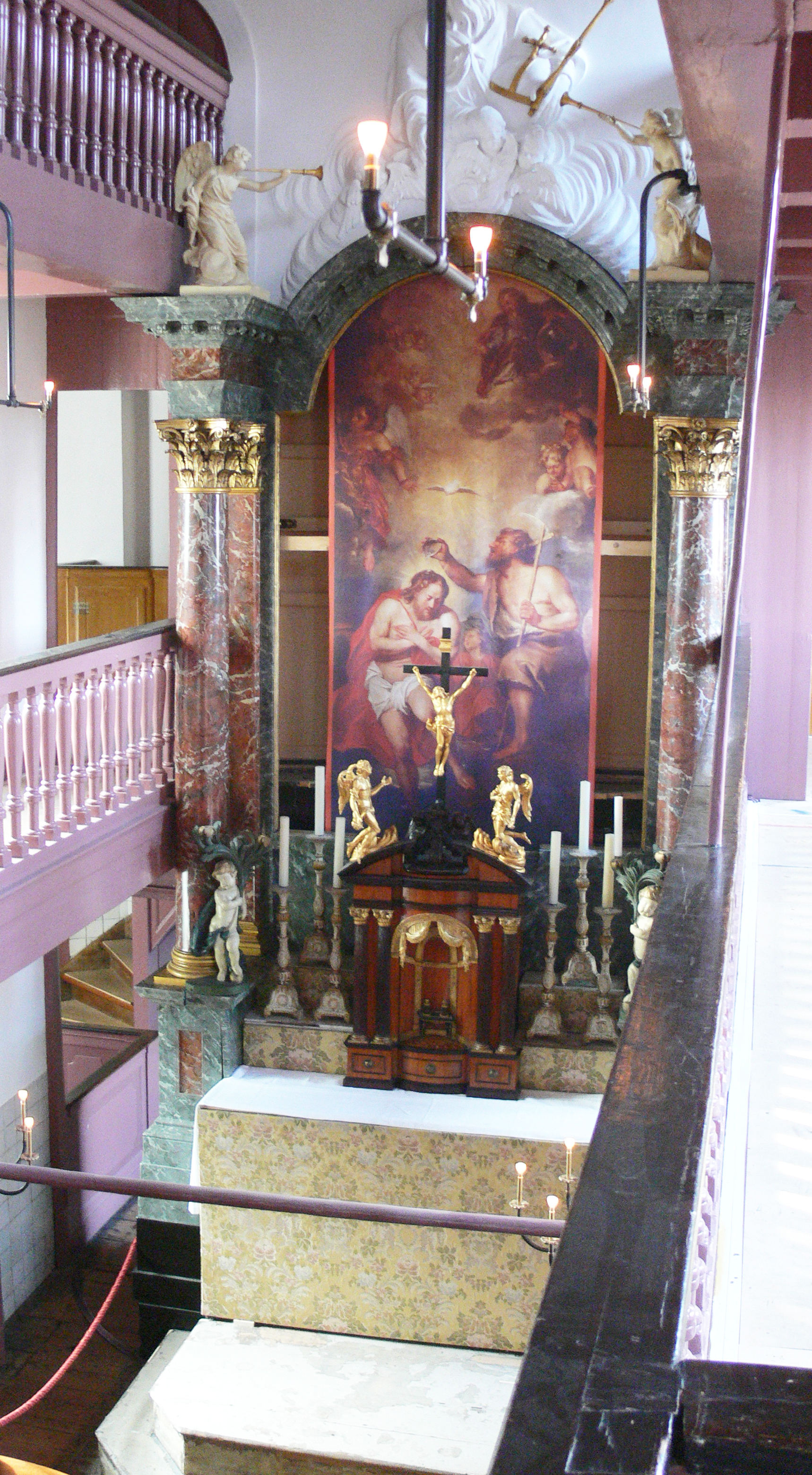 Altar with crucifix and religious paintings in the hidden attic church of Museum Amstelkring, featuring marble columns and golden angel statues.