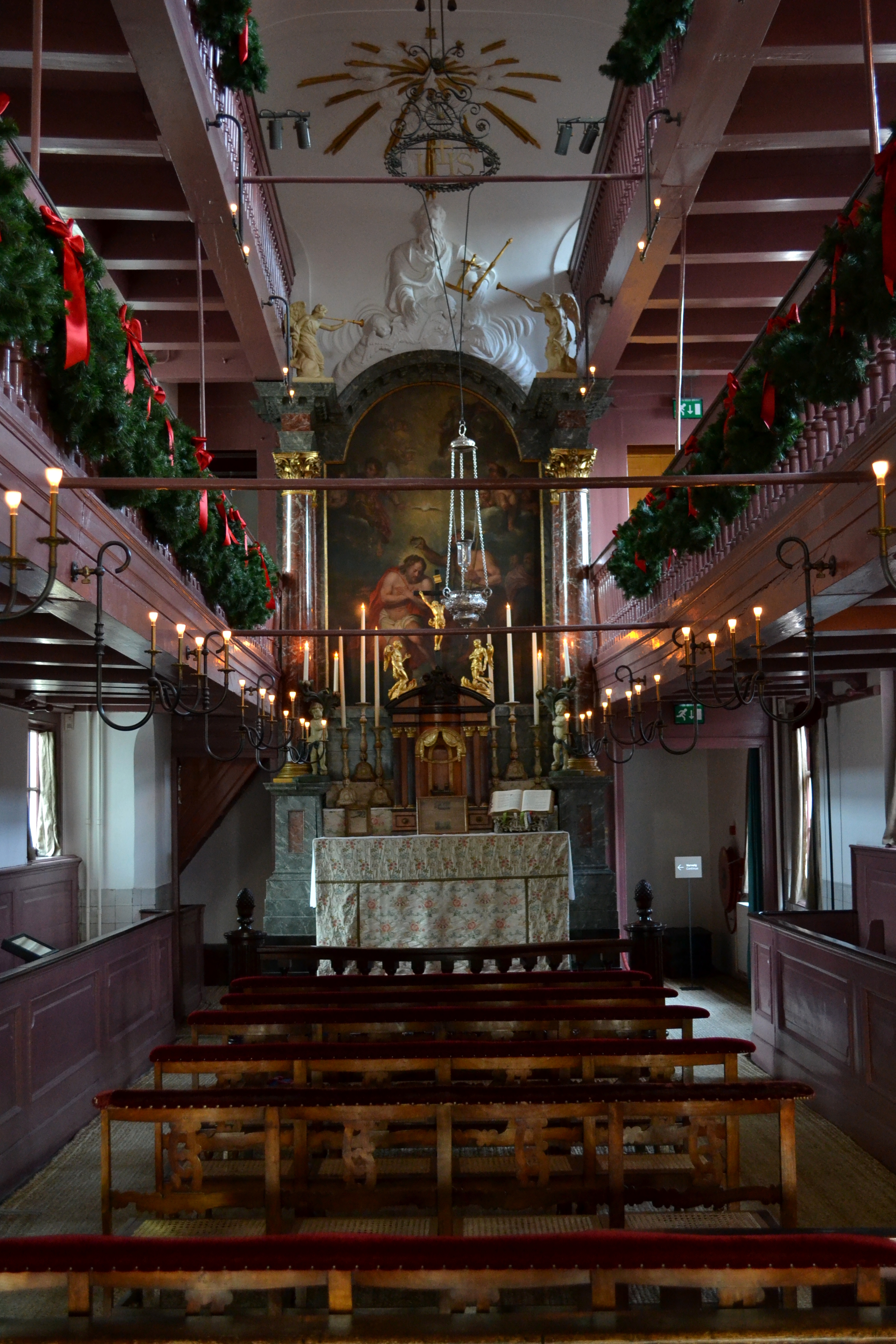 Interior of a hidden church with wooden pews, ornate altar, and festive garlands with red ribbons lining the balconies
