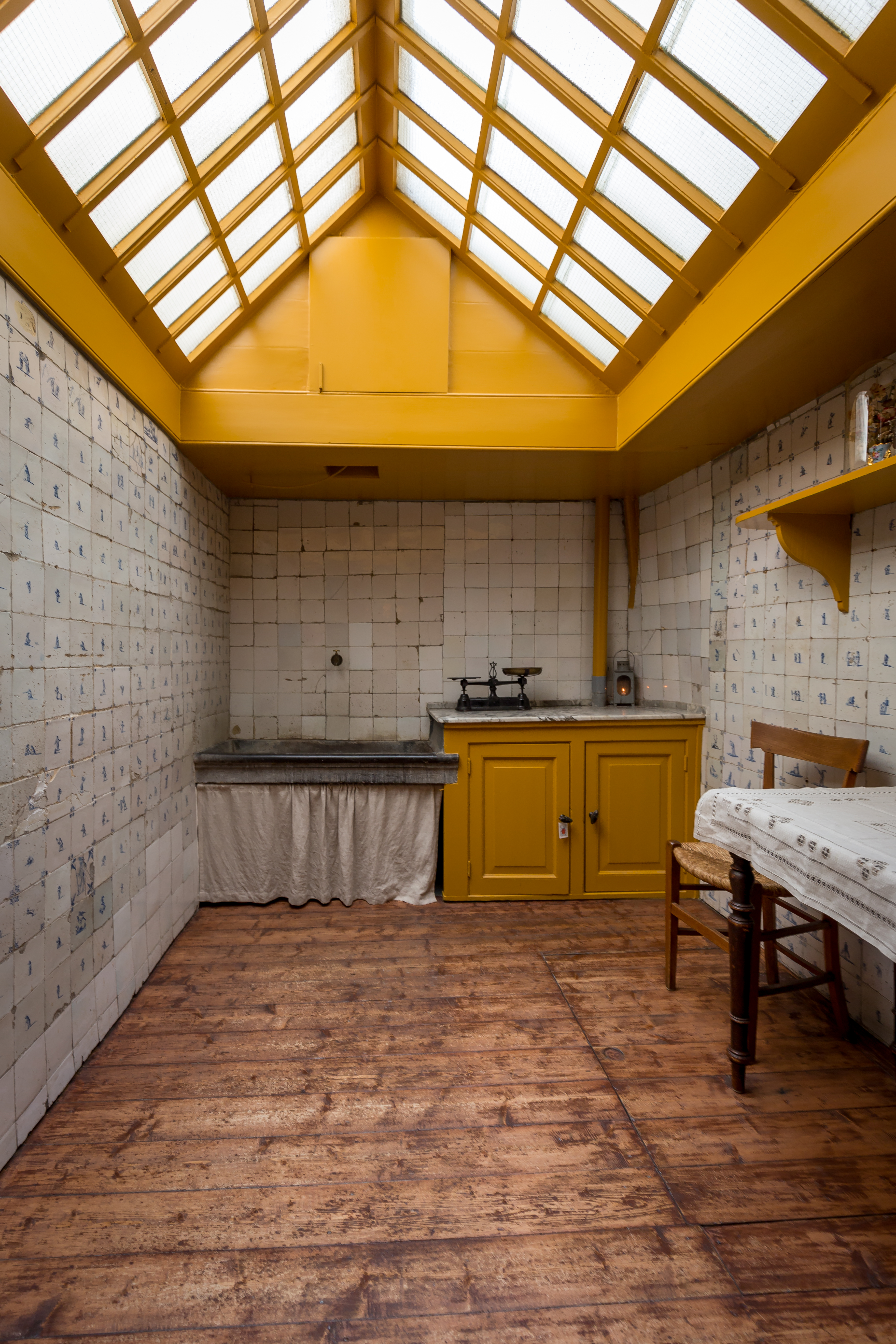 Historical room with wooden floor, yellow-painted ceiling beams, white tiled walls, and skylight at Museum Amstelkring
