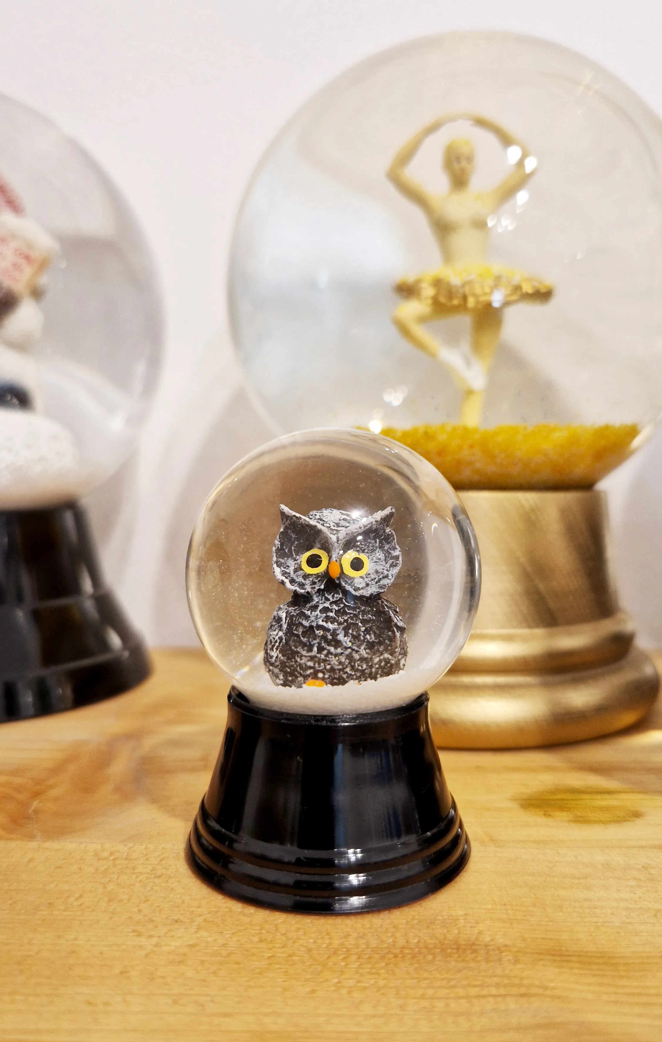 A snow globe with an owl figure inside, displayed on a wooden surface alongside other snow globes.
